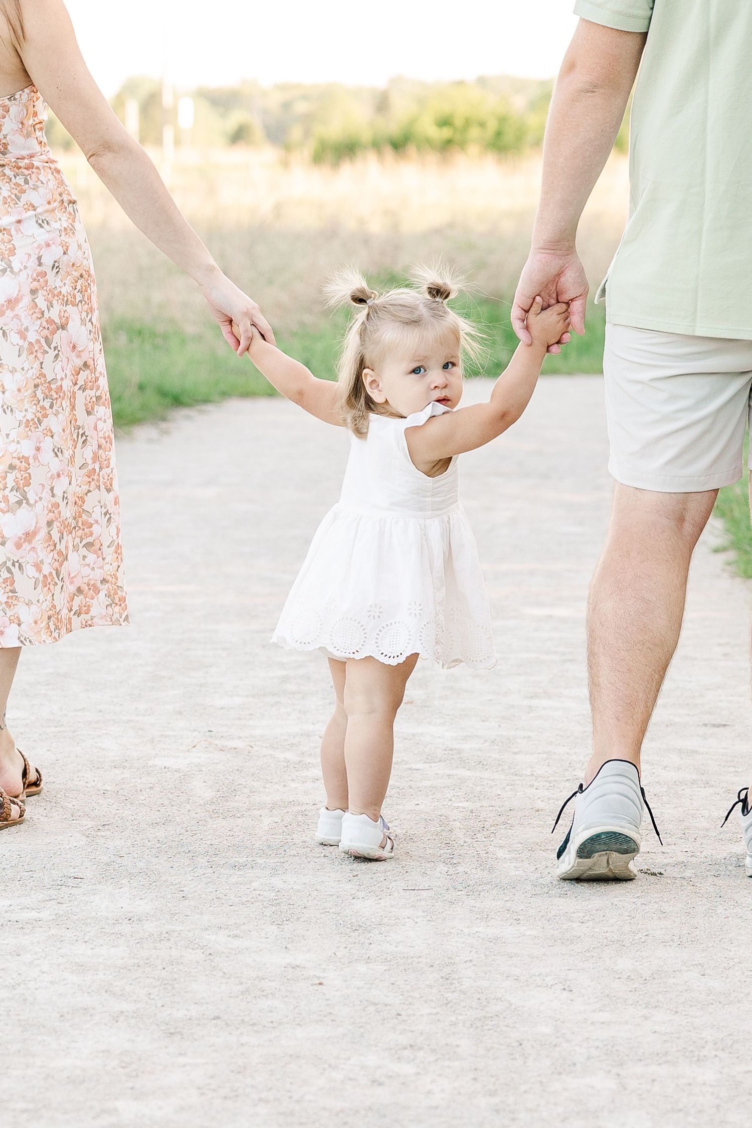 Little one in white dress holding hands while walking on a path outdoors.