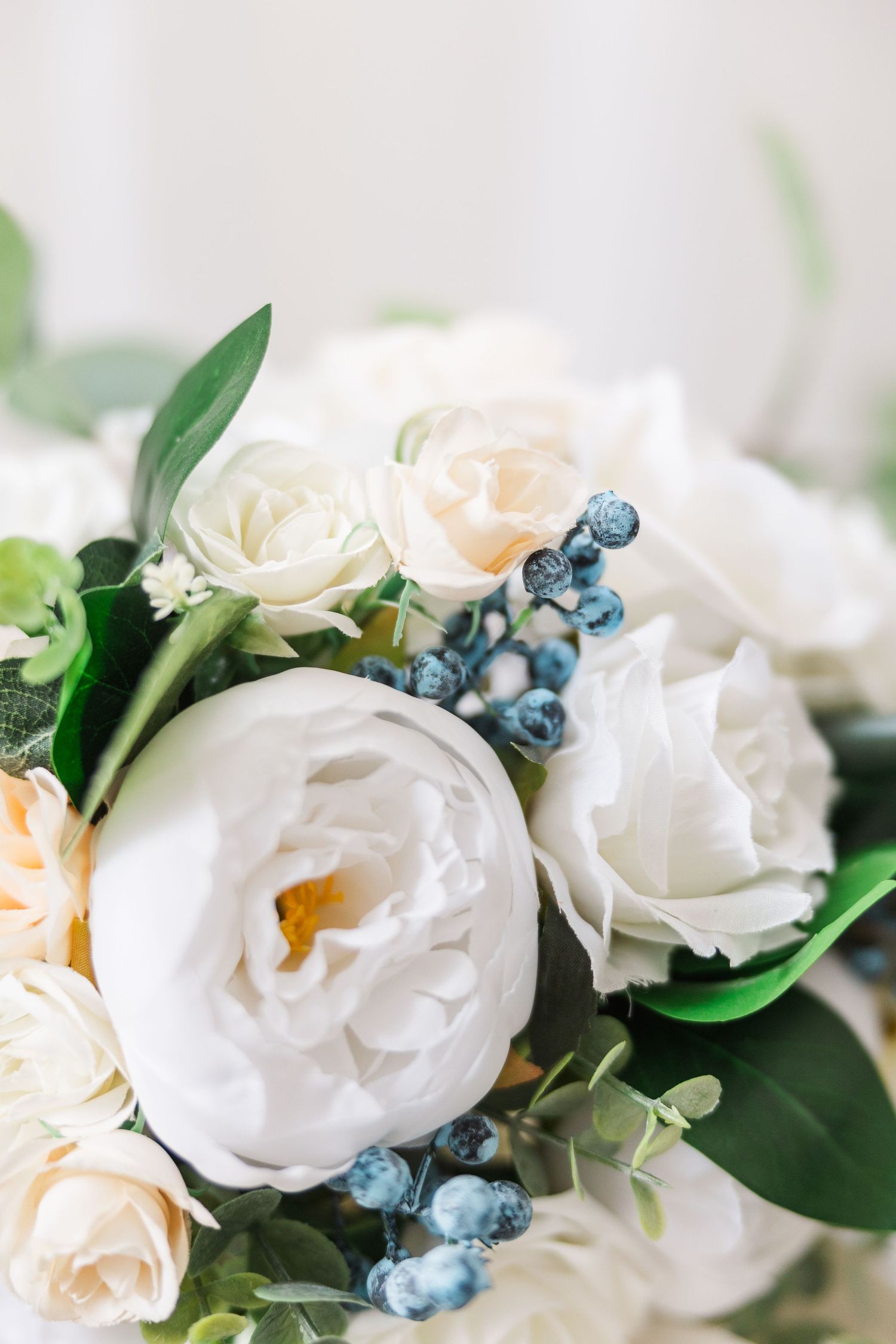 Romantic bouquet featuring white peonies, cream roses, and blue berries with green foliage.