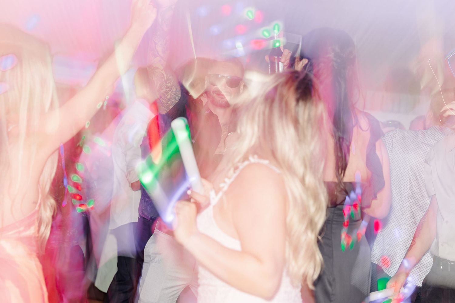 Bride dancing with glowing light sticks at a lively wedding reception party.