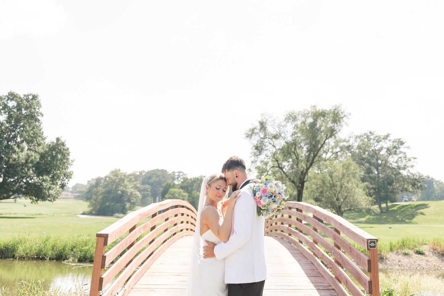 Bride and groom sharing romantic moment on wooden bridge surrounded by lush greenery.