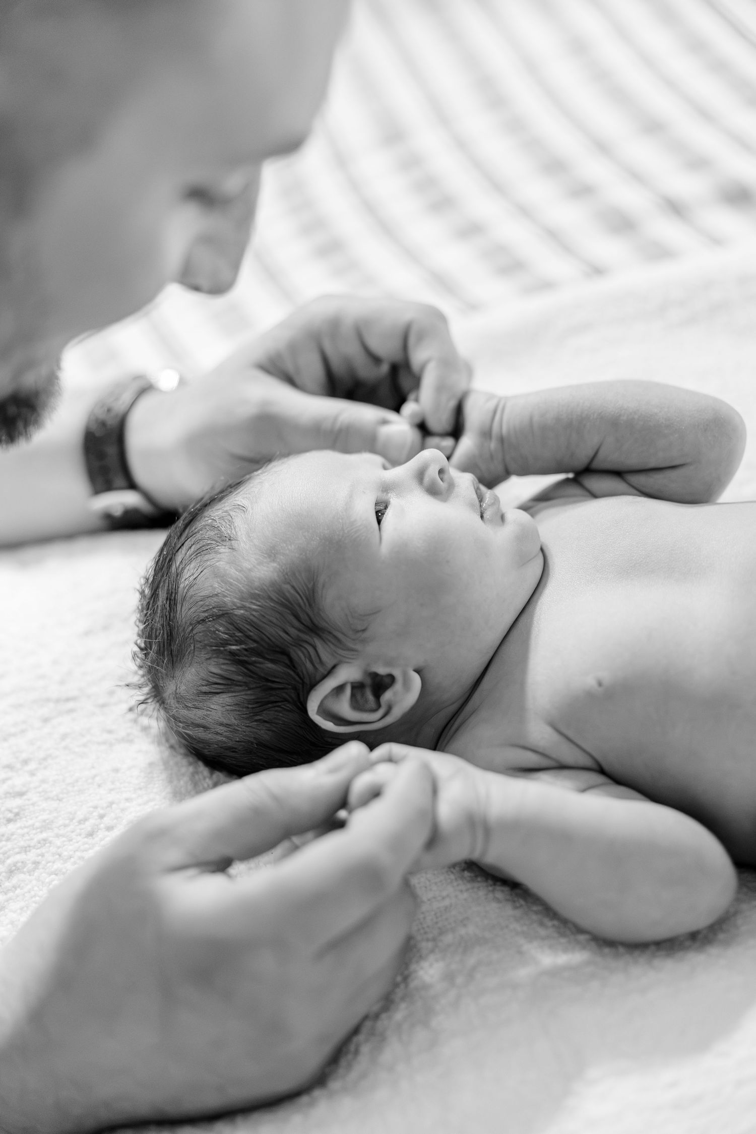 Black and white photo of a father gently holding his alert newborn baby lying on a striped blanket.