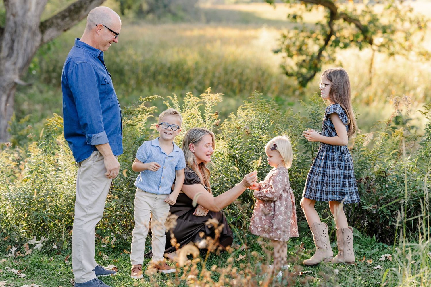 Mom crouching beside her children while Dad looks on during backyard family photos in St. Charles, IL.