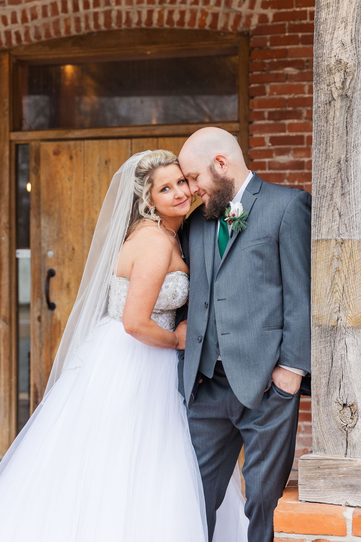 Intimate wedding portrait moment captured against rustic brick wall and wooden doorway.