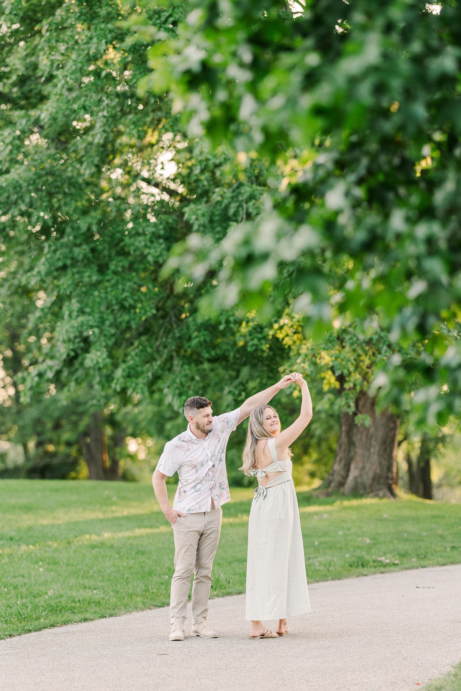 A couple dances playfully together on a winding park path surrounded by lush greenery.