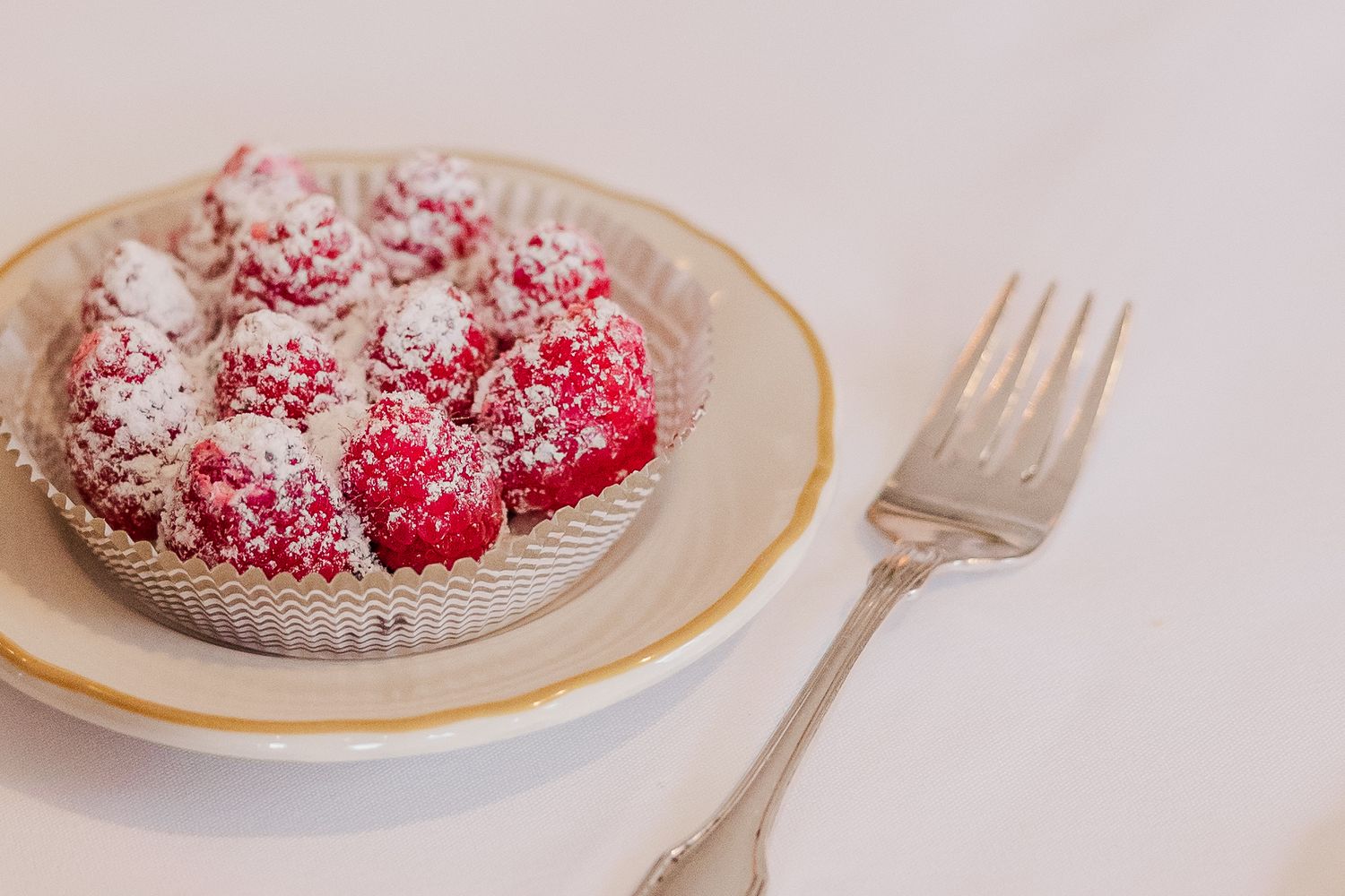 Powdered sugar-dusted red raspberries served on an elegant gold-rimmed plate.