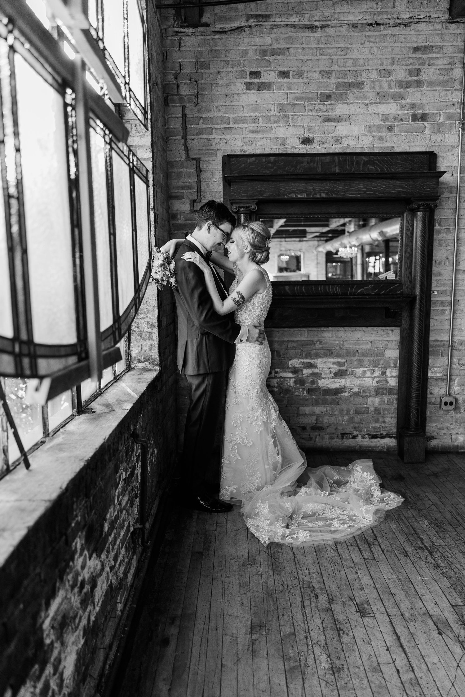 Black and white portrait of couple in wedding attire near vintage windows and brick walls.