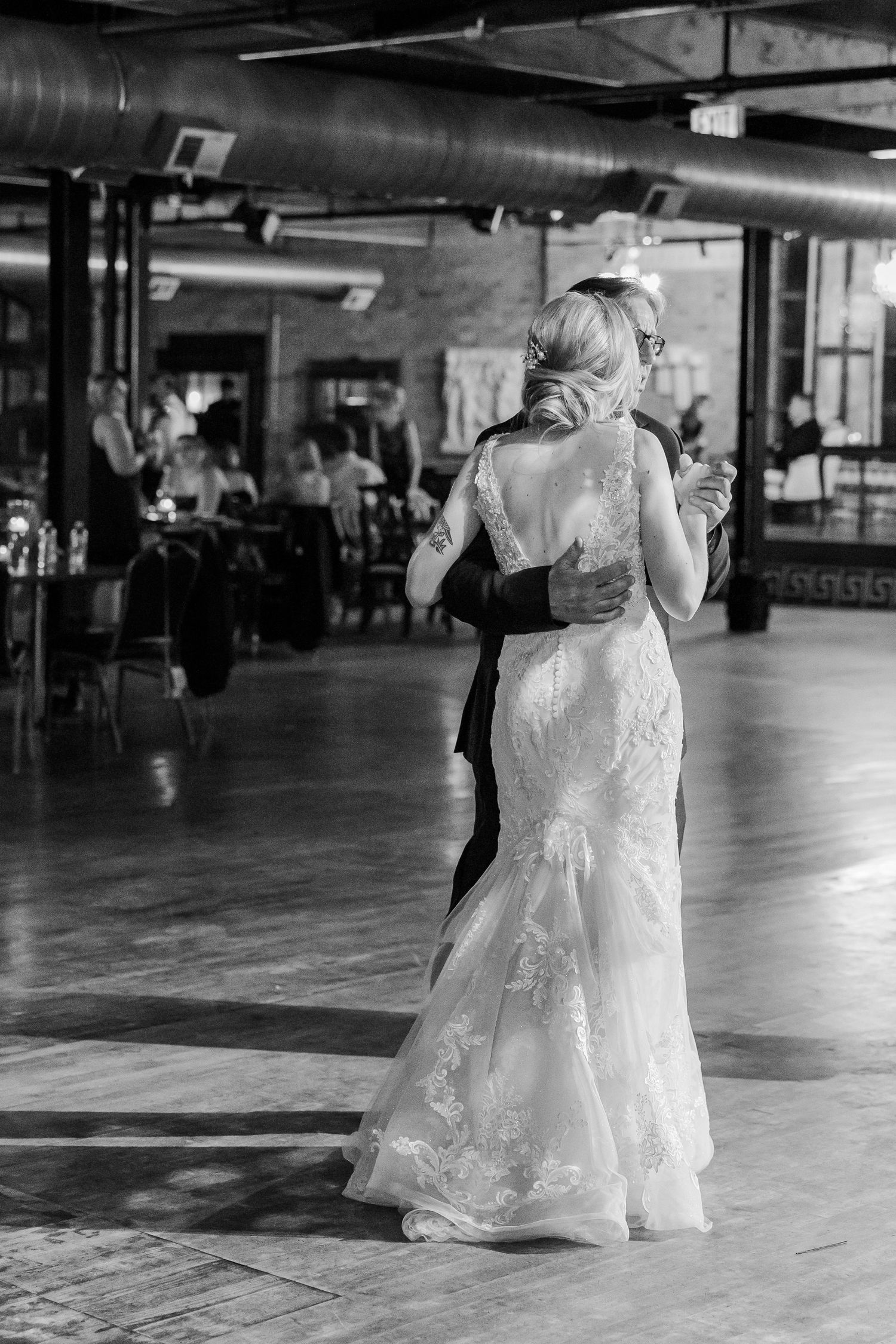 A bride in a lace wedding gown dances in an industrial-style venue.