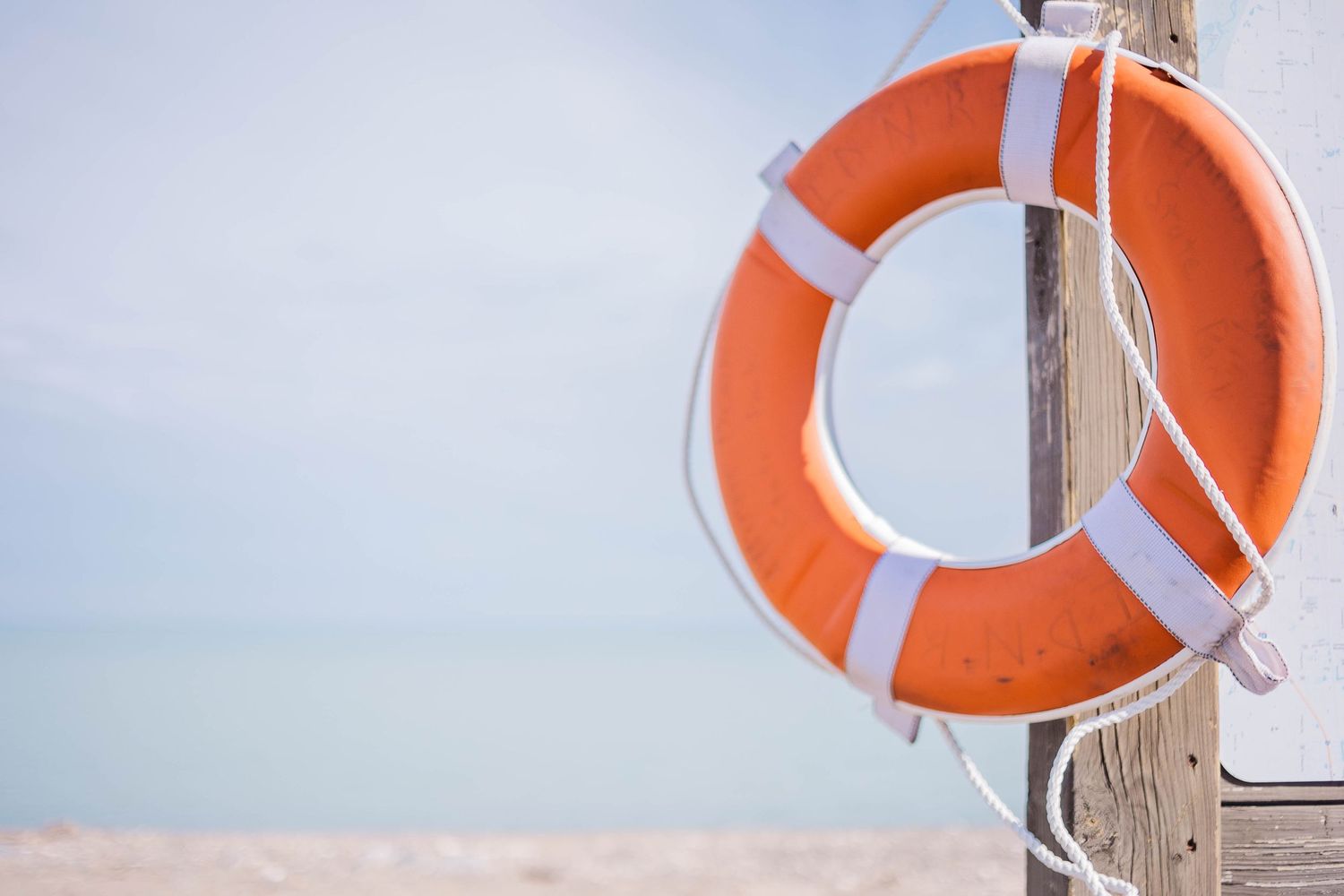 Orange life ring mounted on wooden post against blurred beach background.