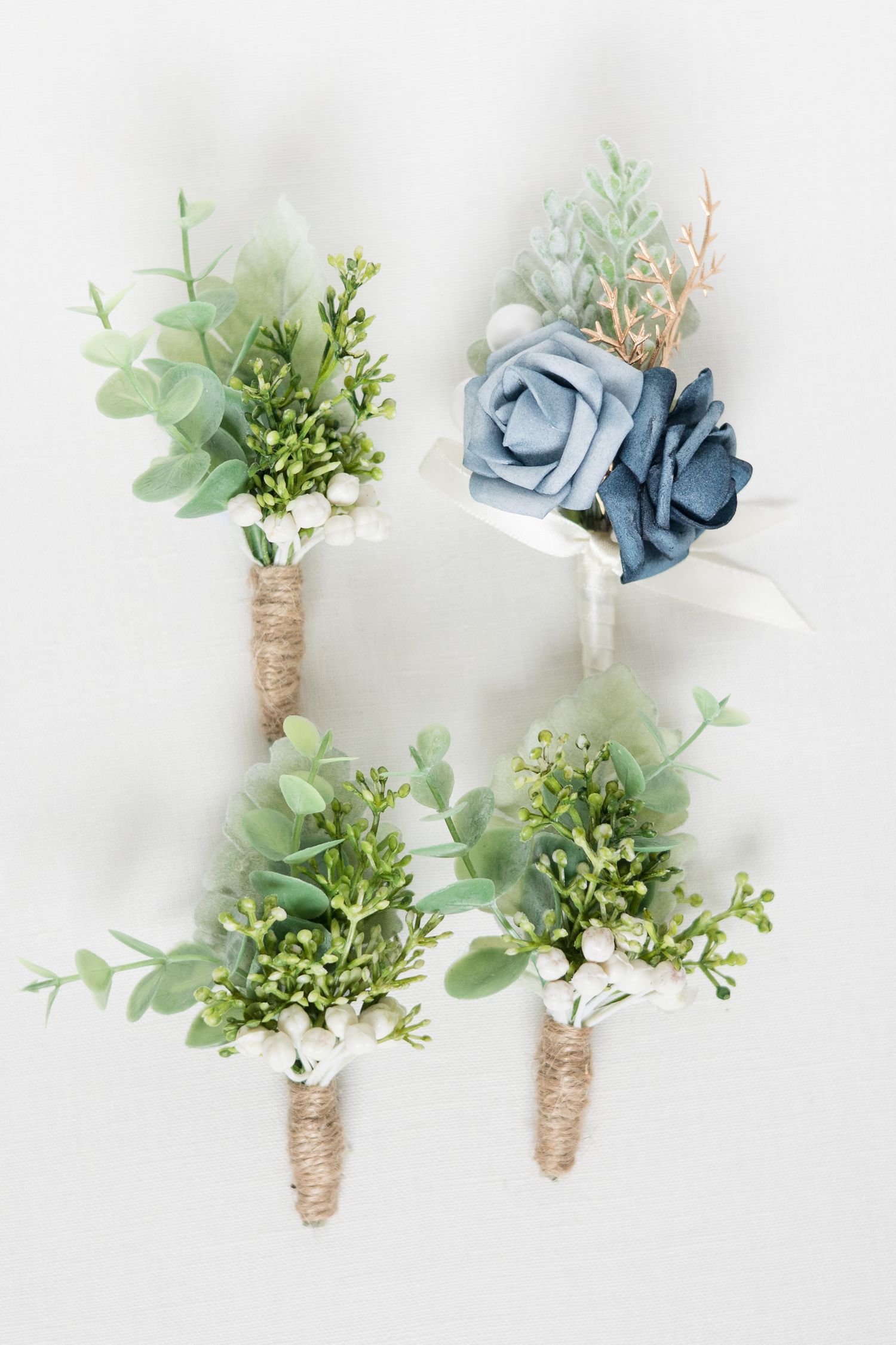 Four boutonnières with blue roses and greenery wrapped in twine.
