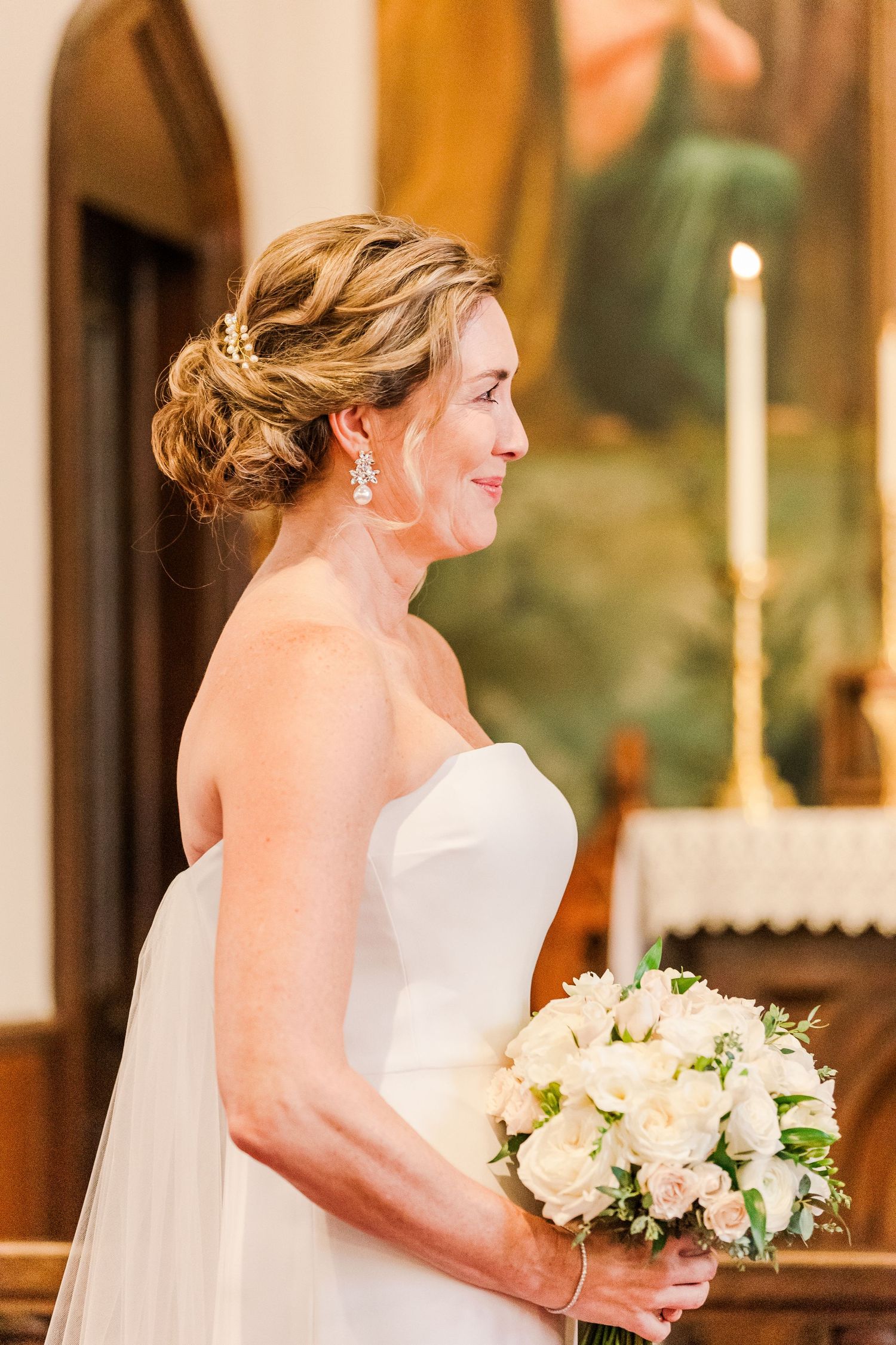 A formal portrait of a bride in a strapless gown holding a white bouquet in a church setting.