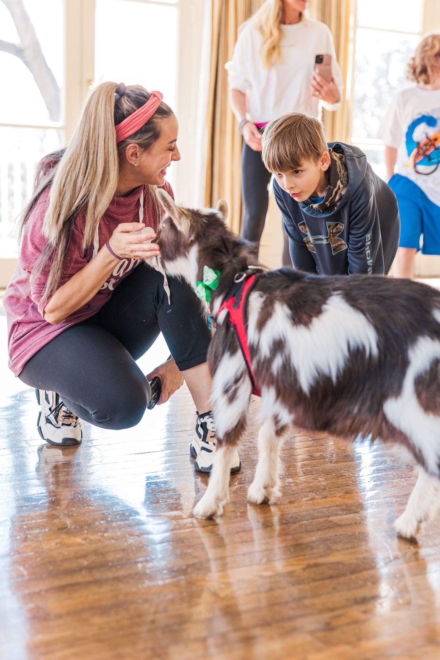 Participants interact with friendly Nigerian Dwarf goats during a goat yoga session on hardwood floors.