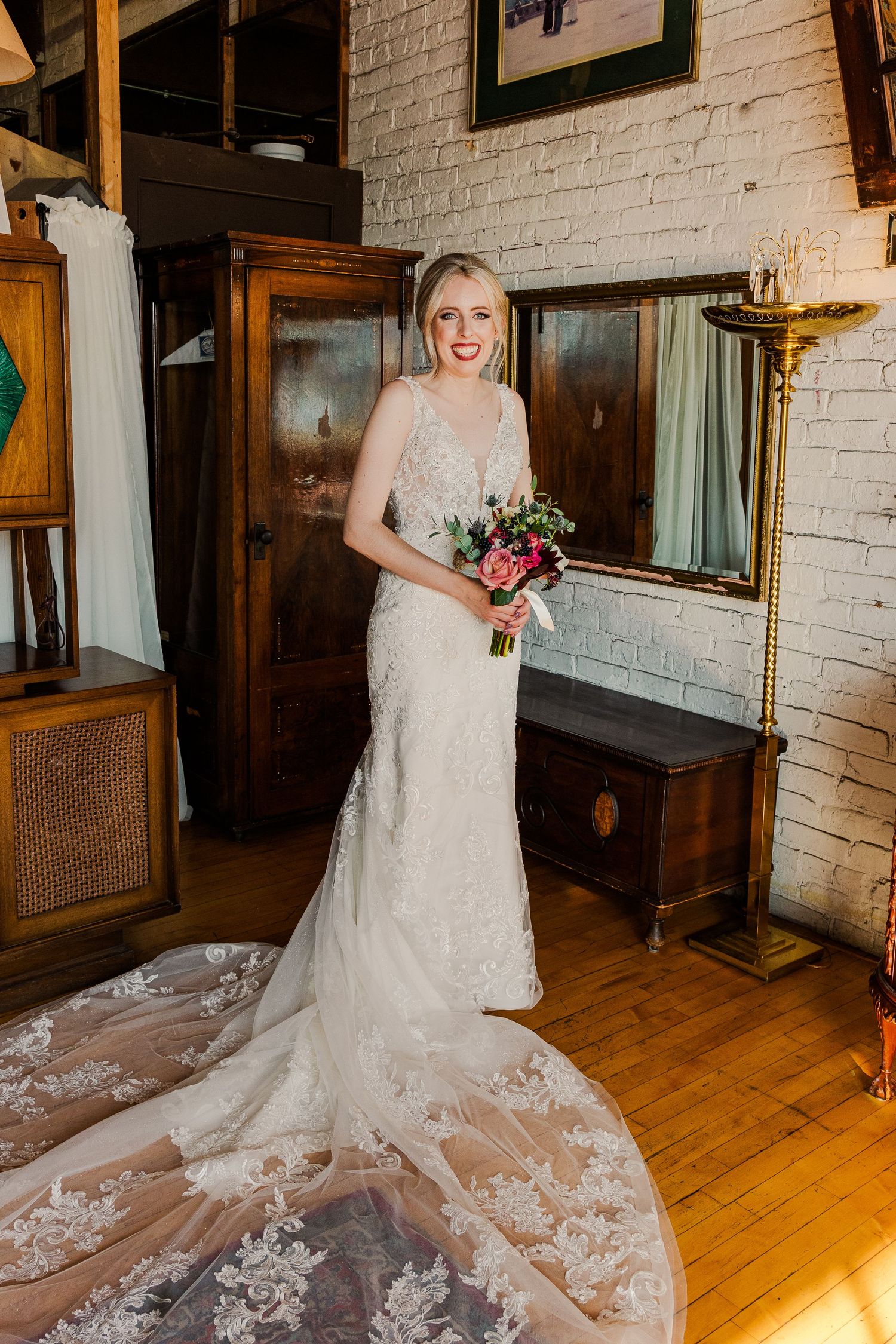 Full-length shot of a stunning lace wedding gown with cathedral train against white brick wall.