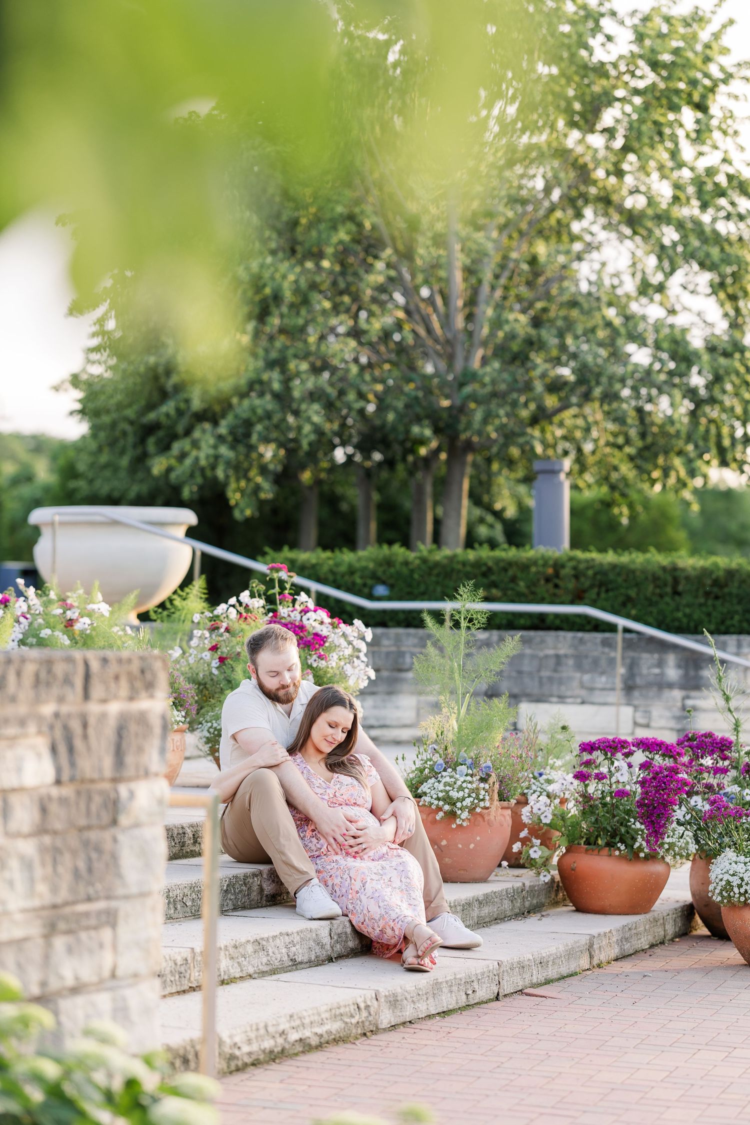 Wide seated maternity portrait of parents-to-be on the garden steps at Cantigny Park in Wheaton