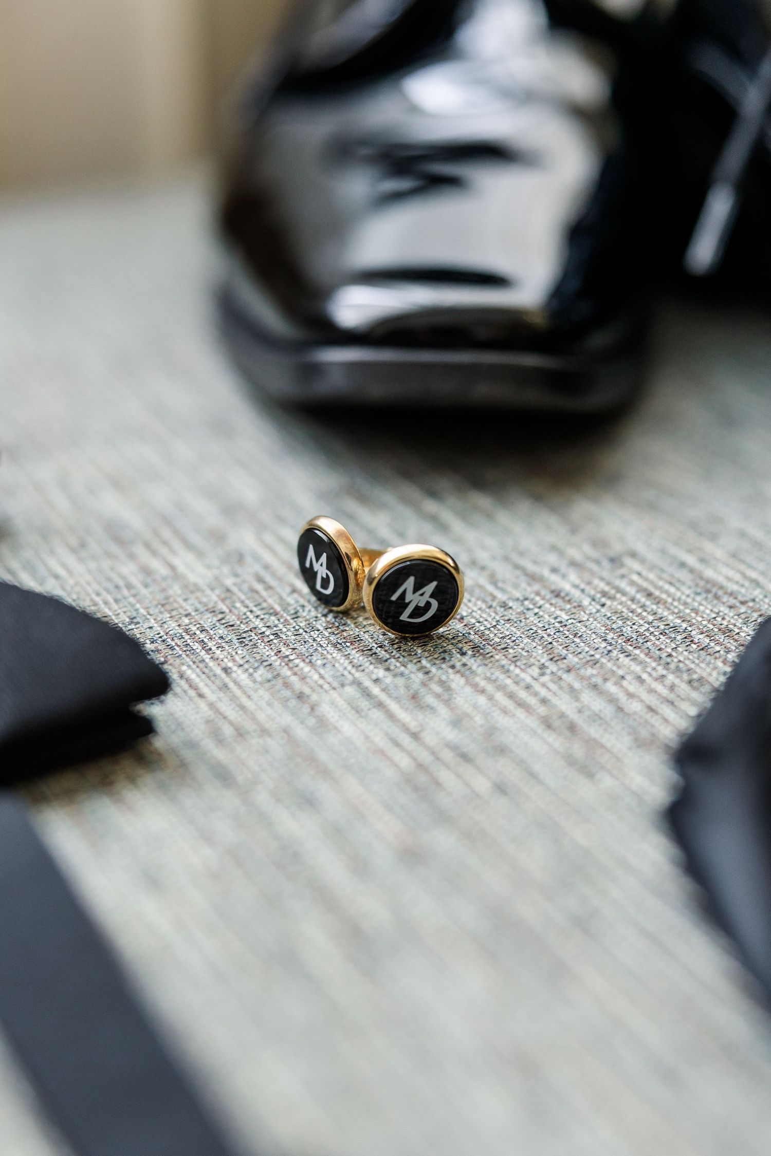Gold and black monogrammed cufflinks displayed near patent leather shoes and bow tie.