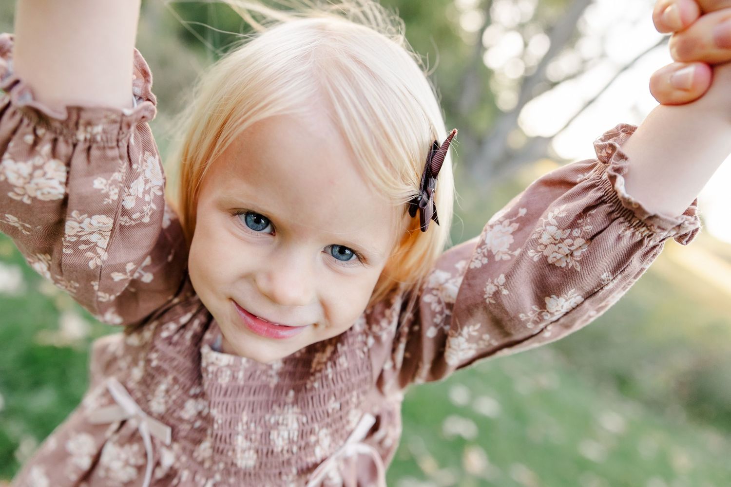 Close-up of a smiling young girl holding an adult's hands during backyard family photos in St. Charles, IL.