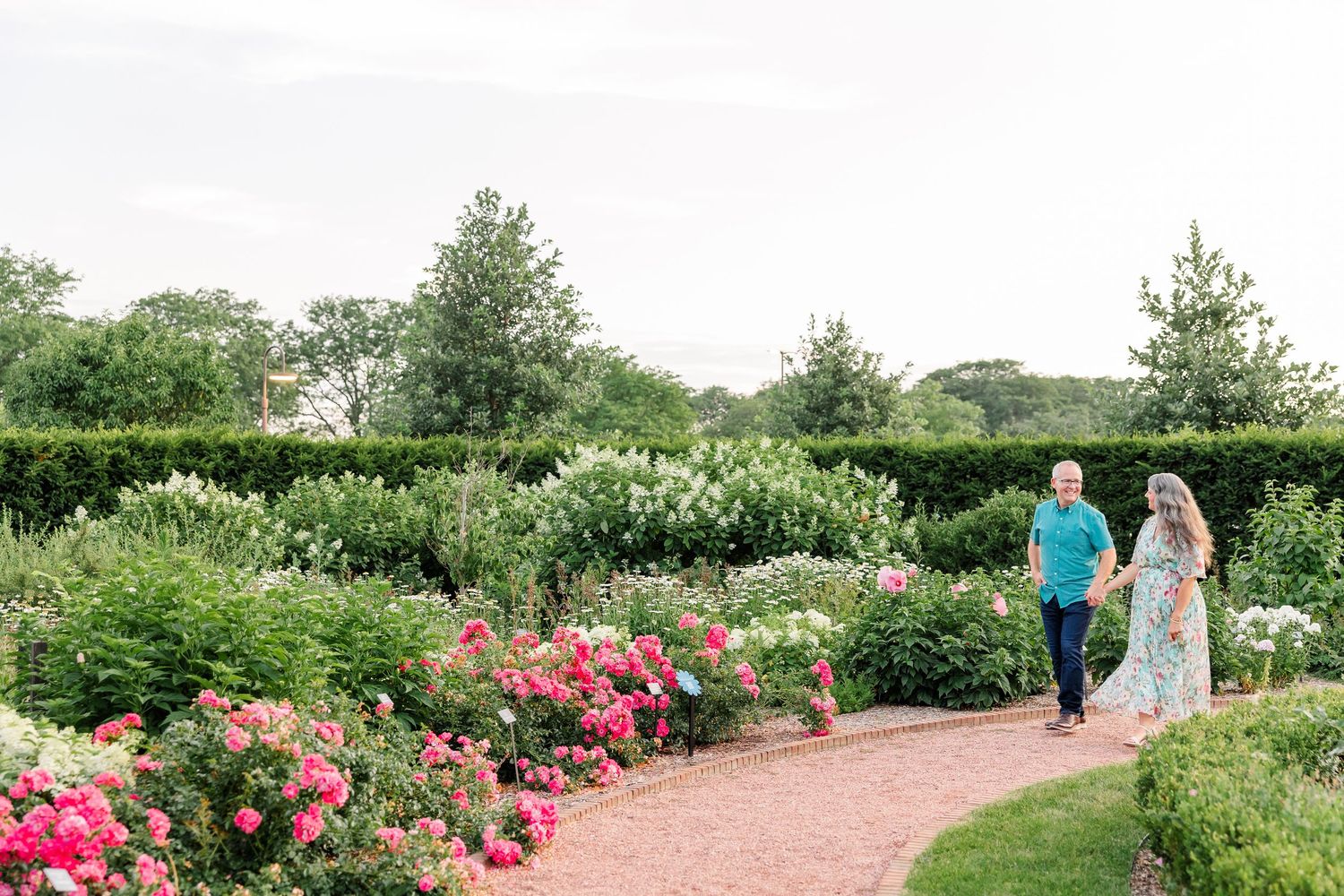 Couple walking hand in hand through a lush garden with colorful roses in bloom.