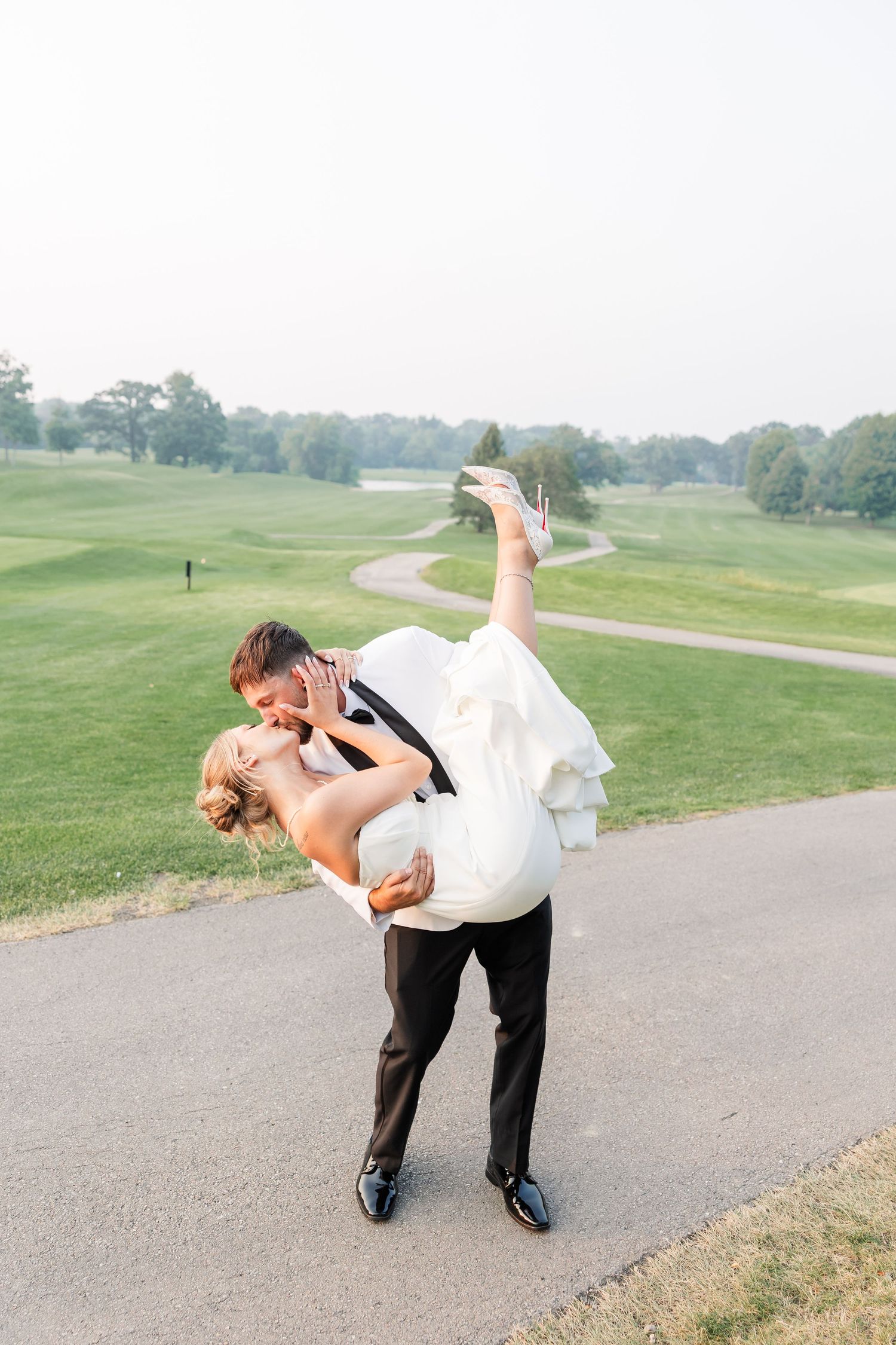 Groom dramatically dipping and kissing bride on golf course path during romantic wedding portrait session.