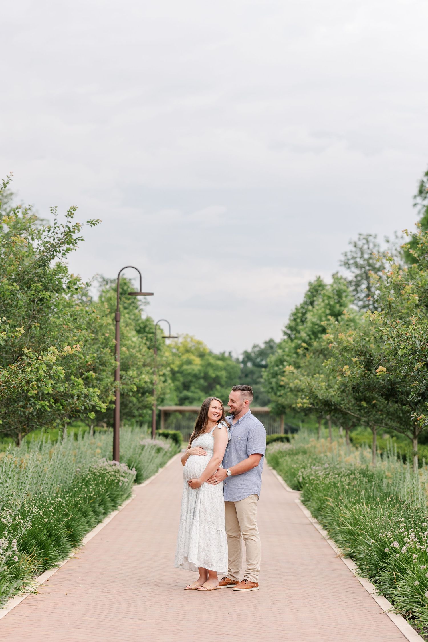 Wide maternity photo of expecting parents on a quiet pathway at Cantigny Park in Wheaton