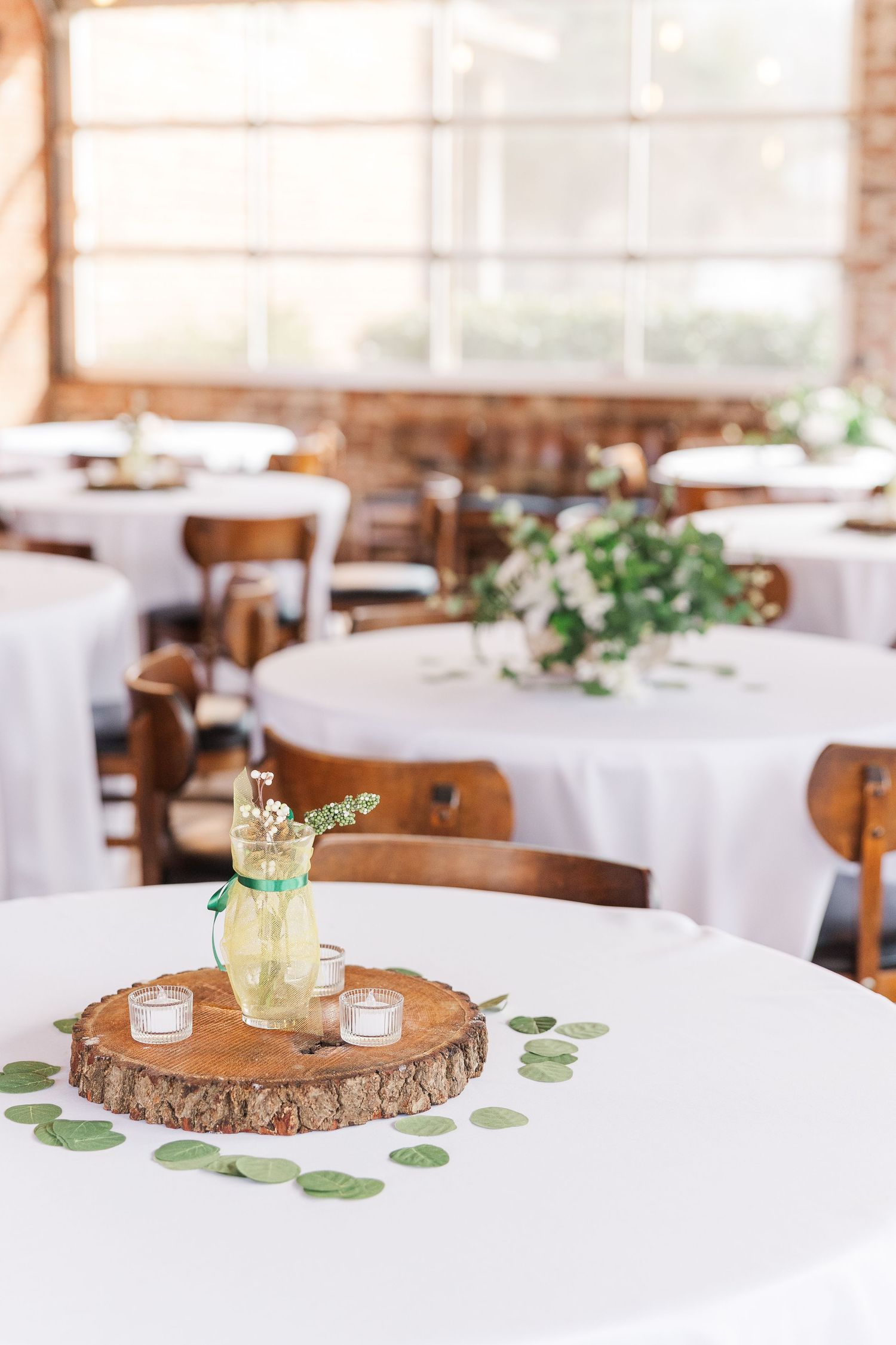 Wedding table centerpiece featuring wood slice charger and greenery on white tablecloth.