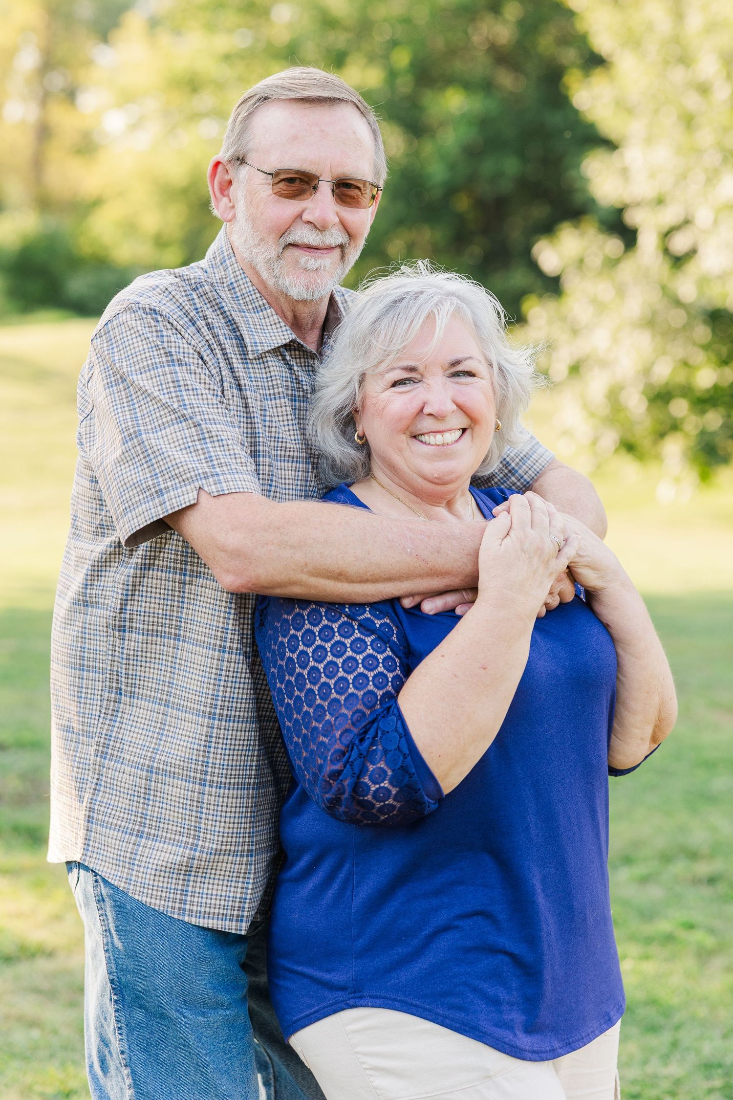 Candid series shows embracing couple in blue top and plaid shirt enjoying playful moment outdoors in sunlit setting.Sorg family portraits at