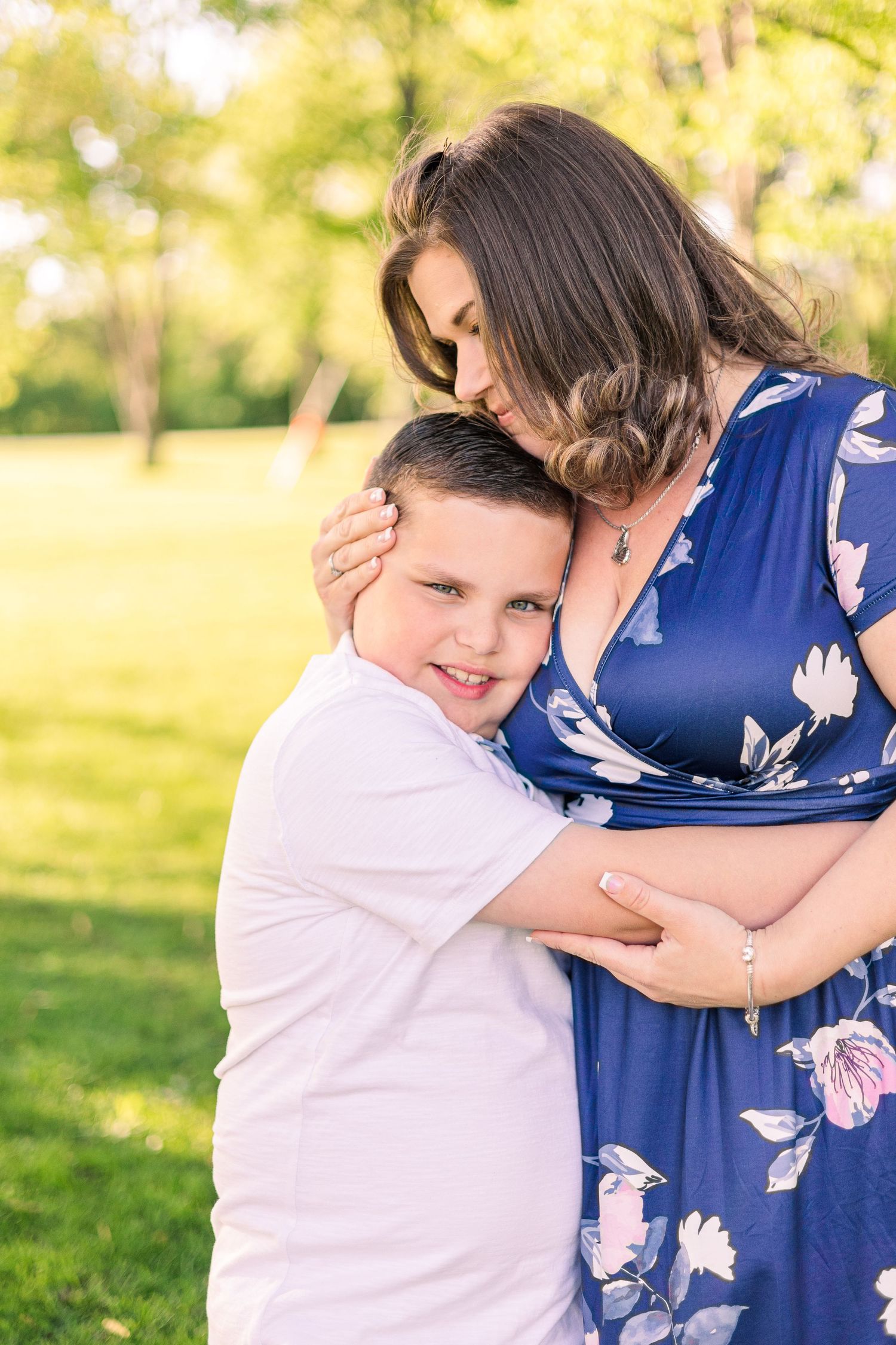 Tender moment captured between two people embracing in a sunlit outdoor setting with floral dress details.