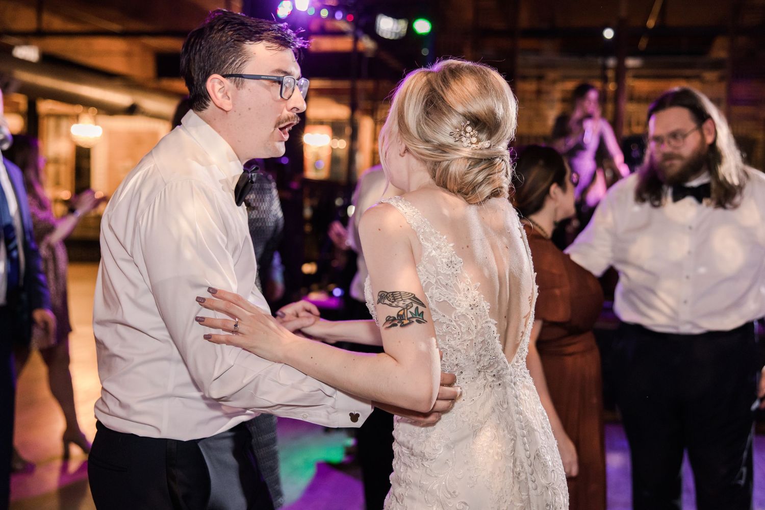 Wedding reception dance party with joyful couple and decorative lighting.