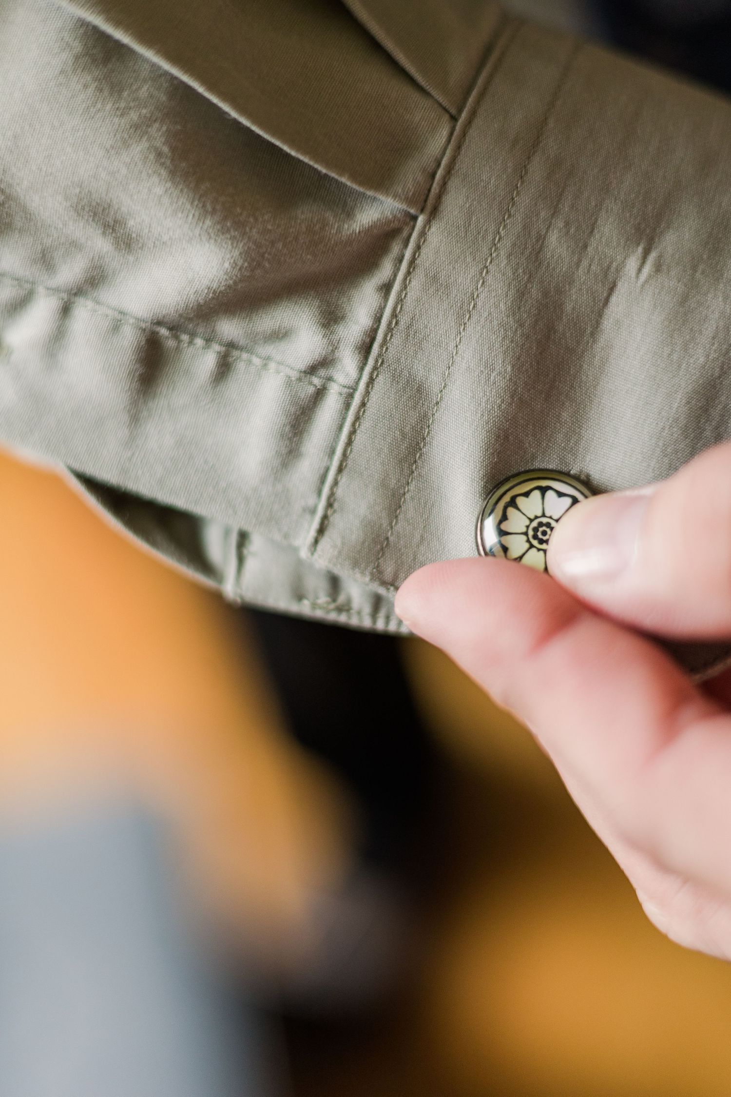 Close-up of fingers adjusting a small button on khaki fabric.