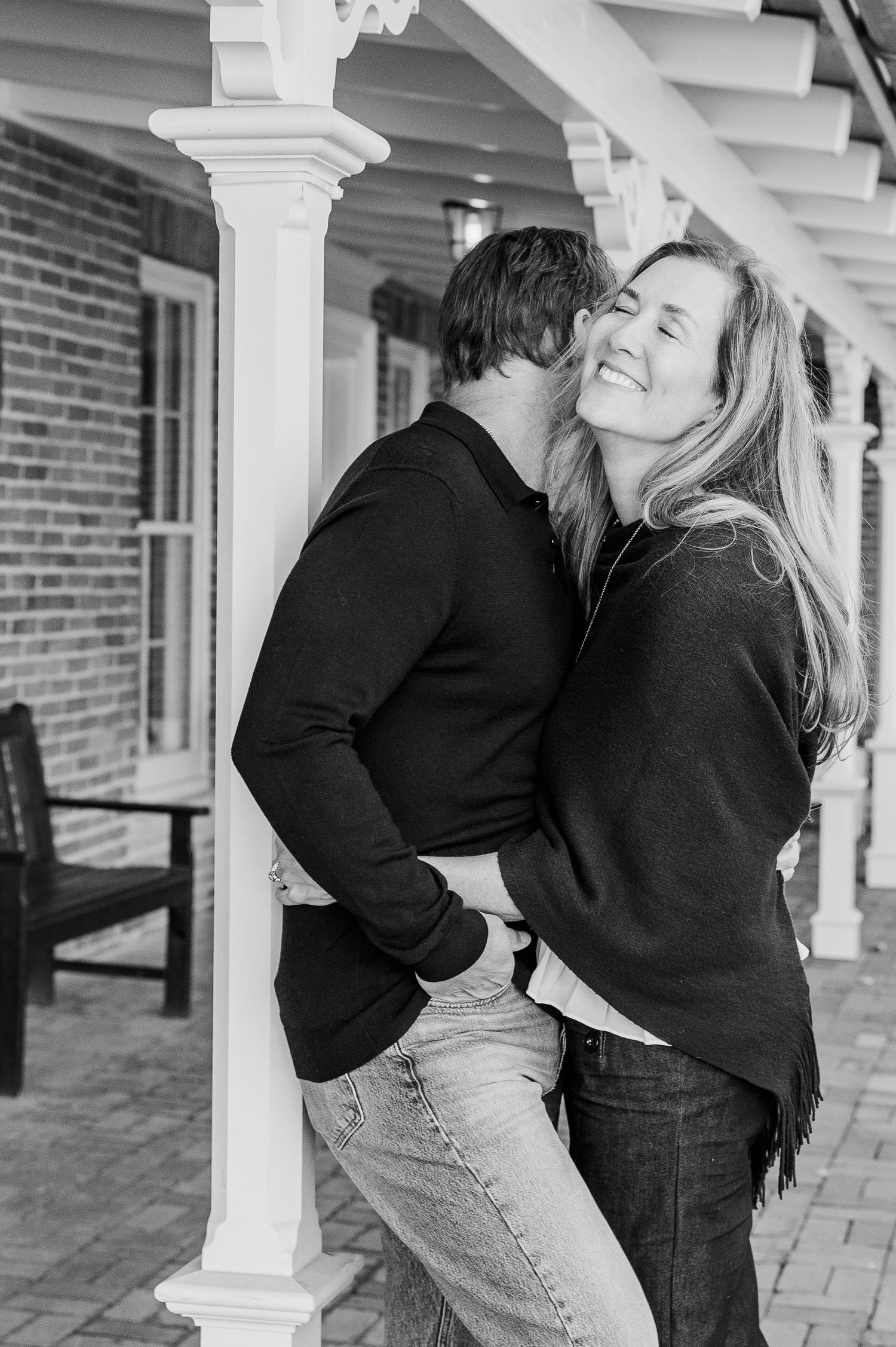 Black and white portrait of couple in casual wear sharing an affectionate moment by columns.