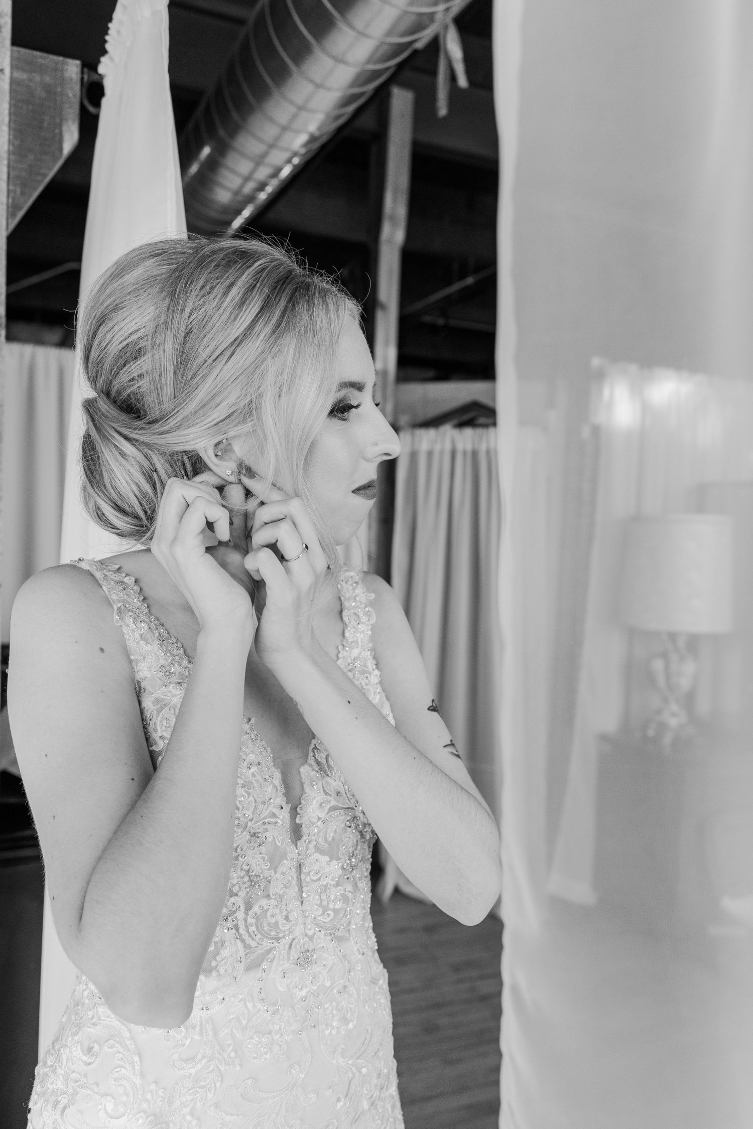 Black and white portrait of bride in lace gown adjusting earrings.