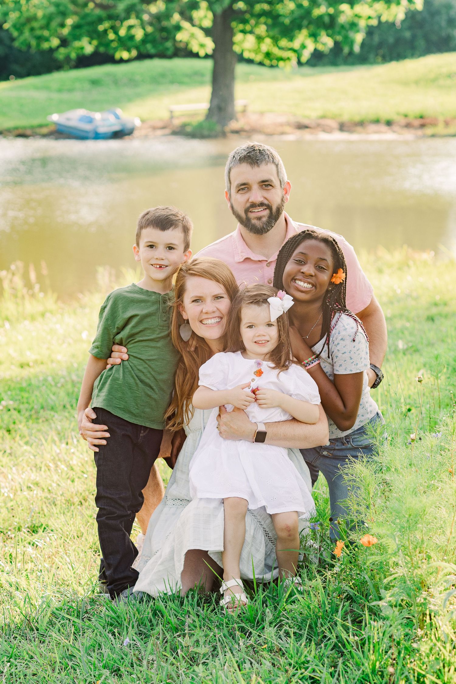 Family portrait outdoors with natural pond and tree in background.