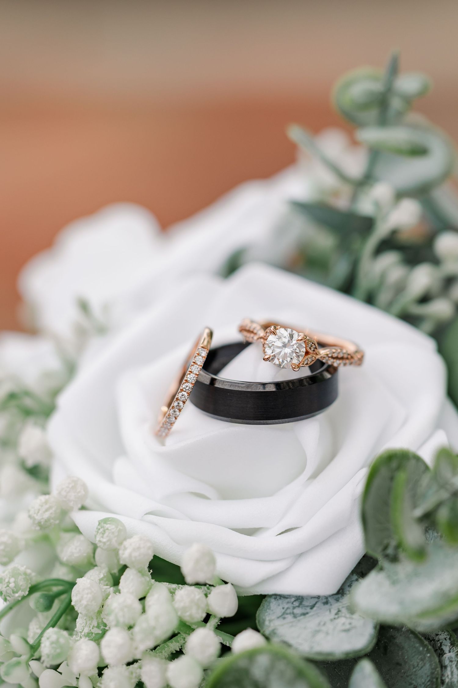 Bride’s engagement ring and wedding band with the groom’s black wedding band resting on her white bouquet.