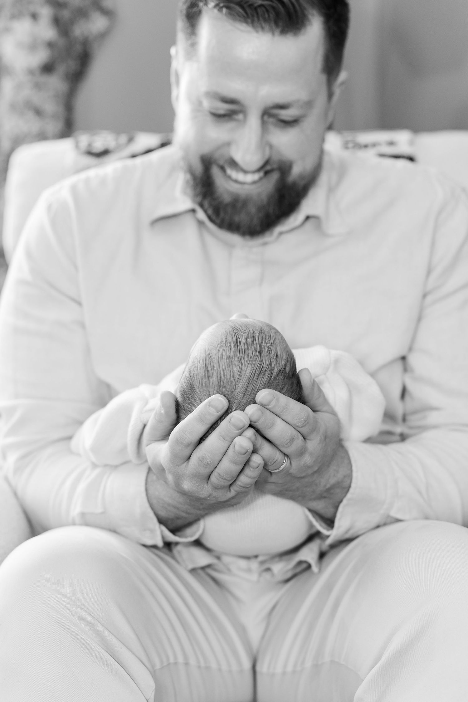 Black and white photo of bearded father smiling while cradling newborn baby's head in hands.