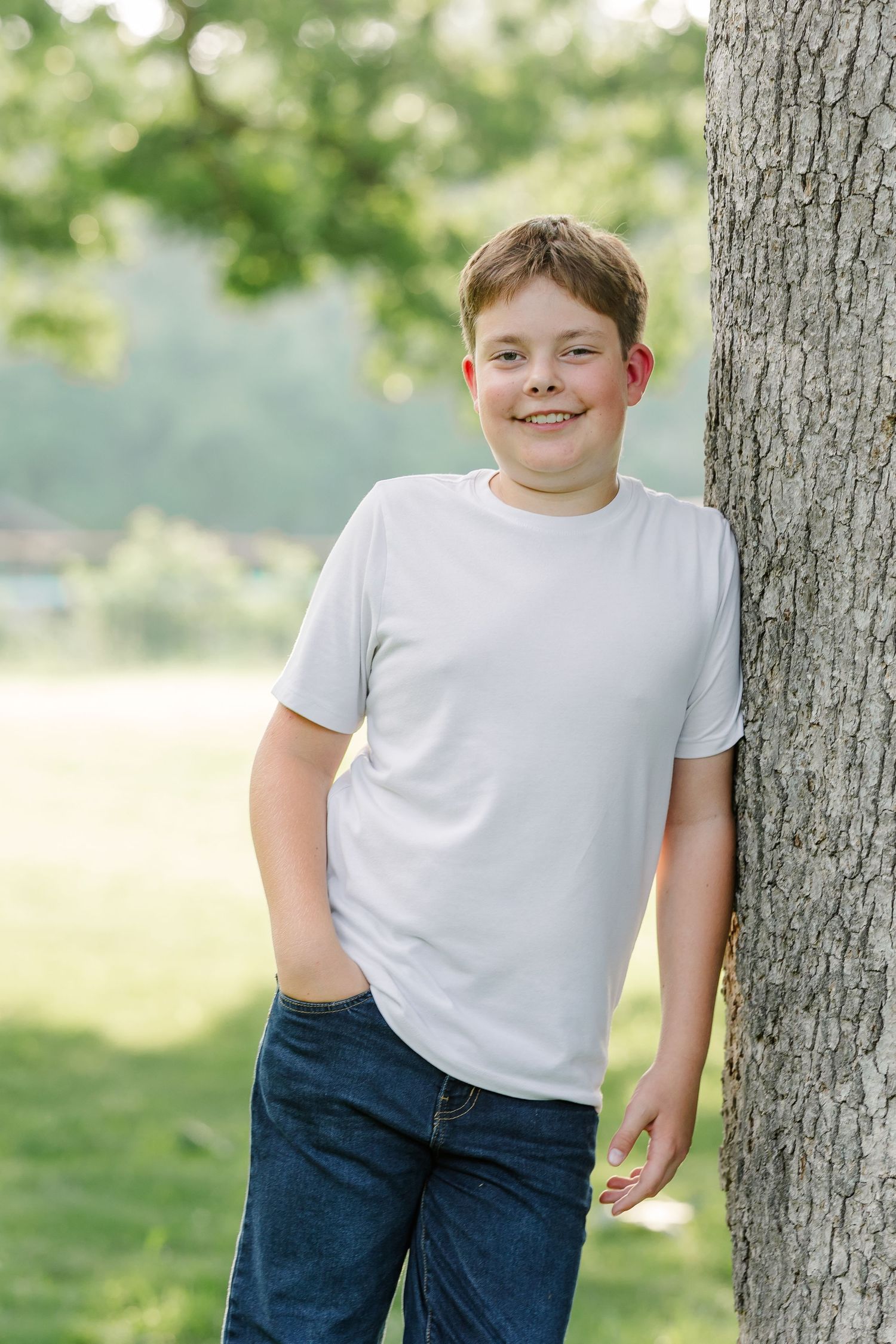 Portrait of a young boy leaning against a tree.