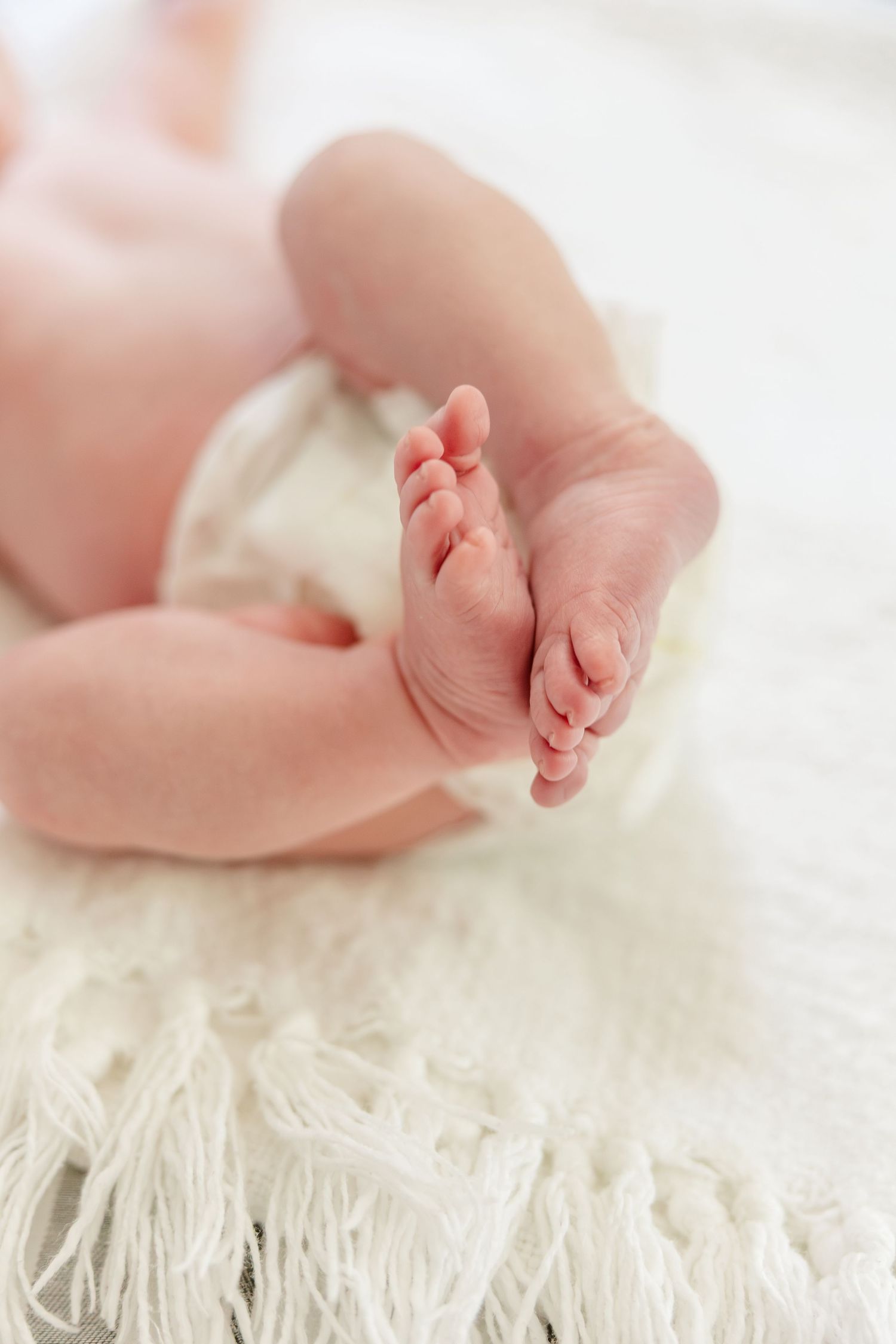 Close-up of tiny newborn baby feet resting on a soft white knit blanket.
