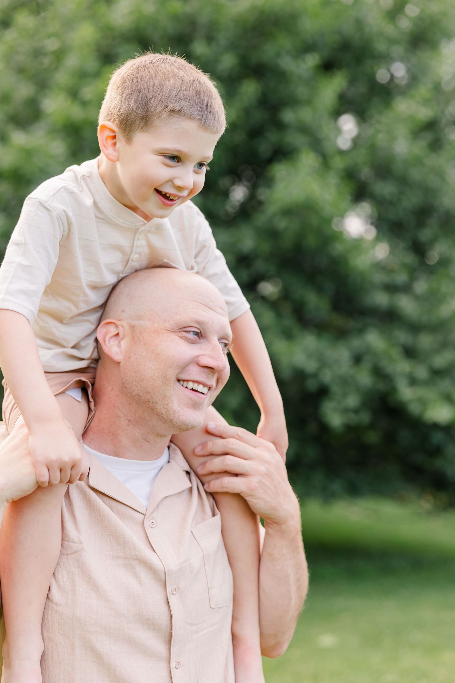 Young boy smiling on his dad’s shoulders during a summer family photo session in Crystal Lake, Illinois.