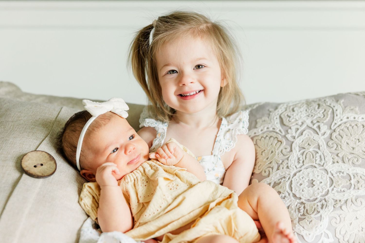 Big sister smiling while snuggling newborn baby girl during an in-home newborn photography session