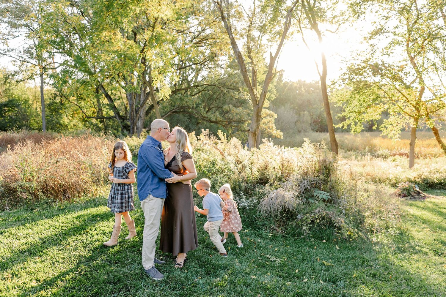 Parents embracing with their three children beside them during golden backyard family photos in St. Charles, IL.