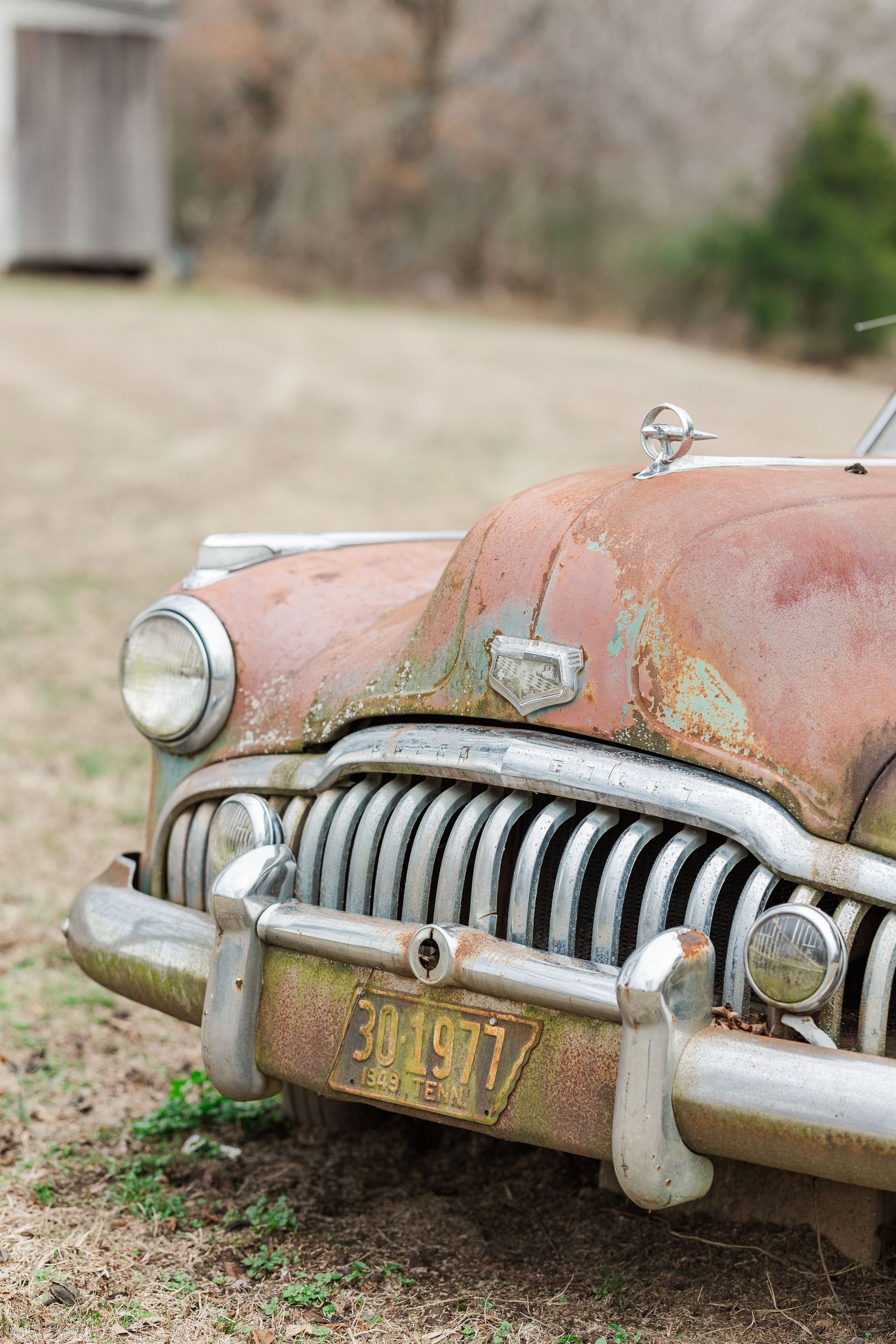 Close-up detail of weathered vintage car grille and headlight with patina finish.