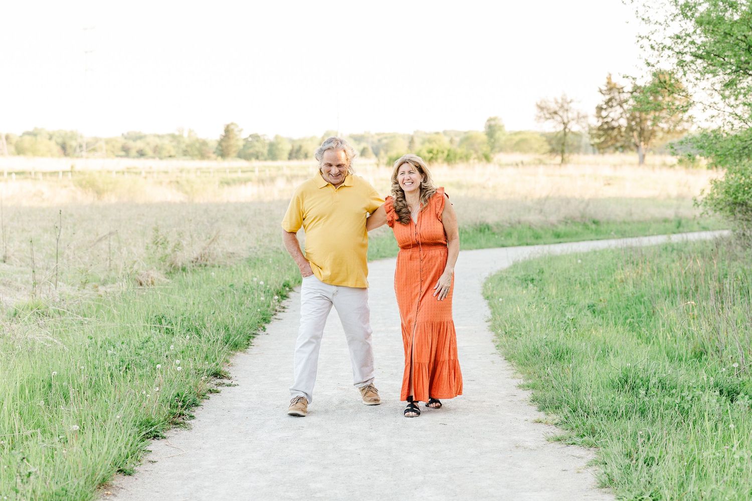 A couple in bright yellow and orange outfits walking together on a sunlit path.