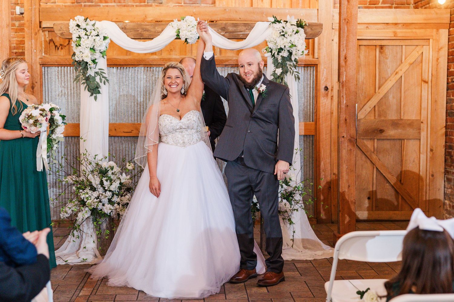 Wedding celebration with a white floral arch backdrop in a rustic wooden venue.