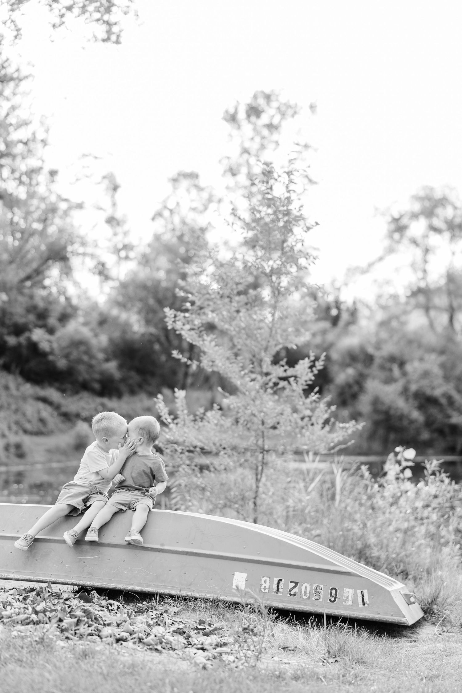 Two children wearing winter coats lay on a wooden platform in a wooded area on a winter day.