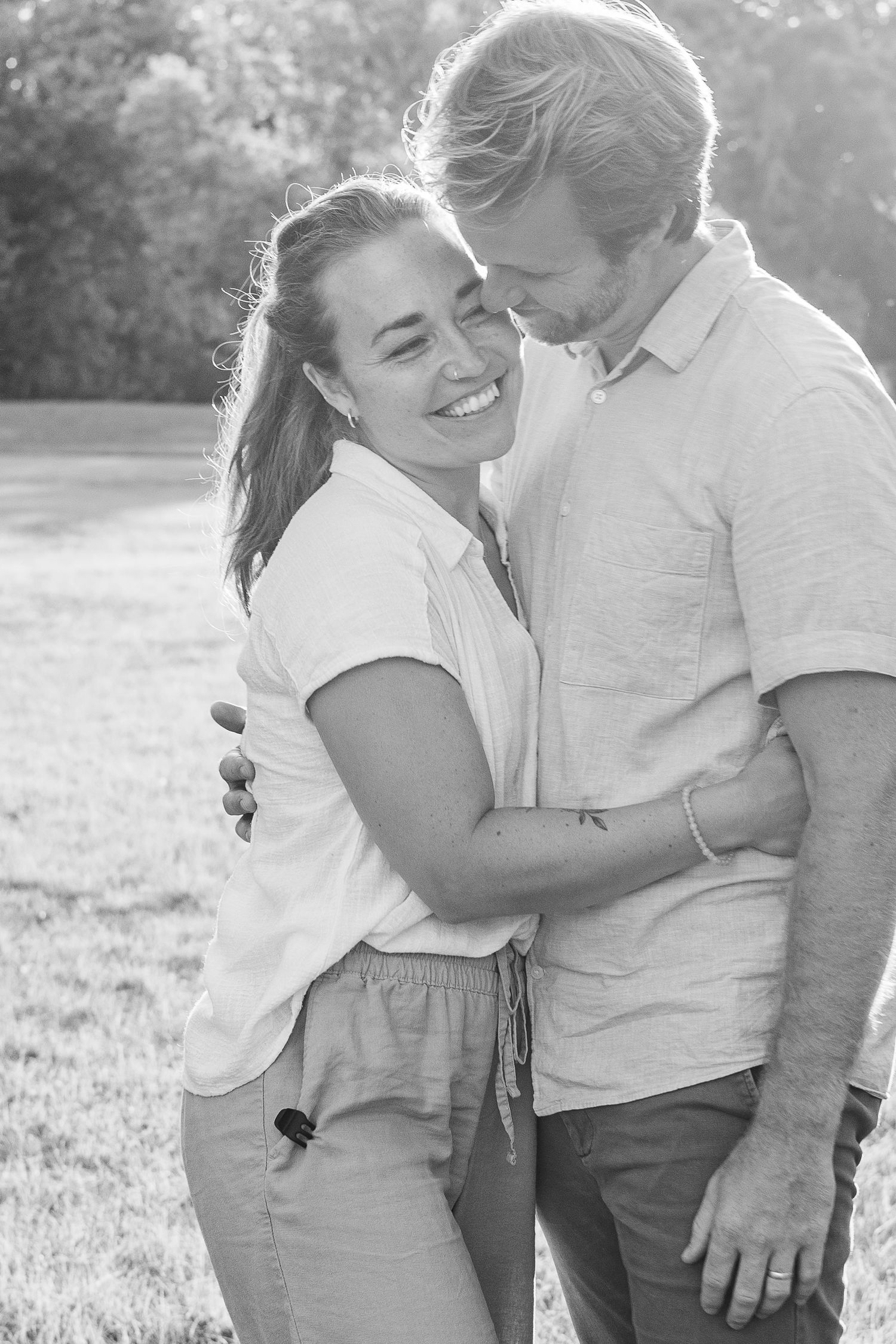 An intimate black and white portrait of a couple embracing and laughing together outdoors.
