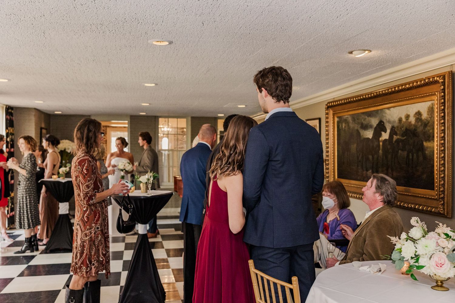 Guests mingling at an elegant indoor reception with checkered floor and ornate decor.