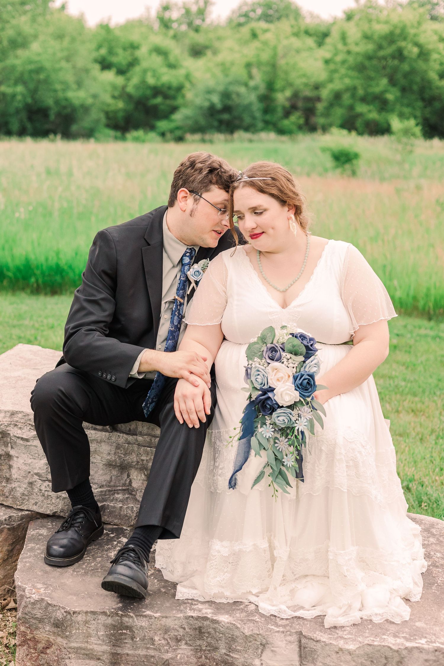 Couple shares intimate moment while sitting on stone in rustic outdoor setting.