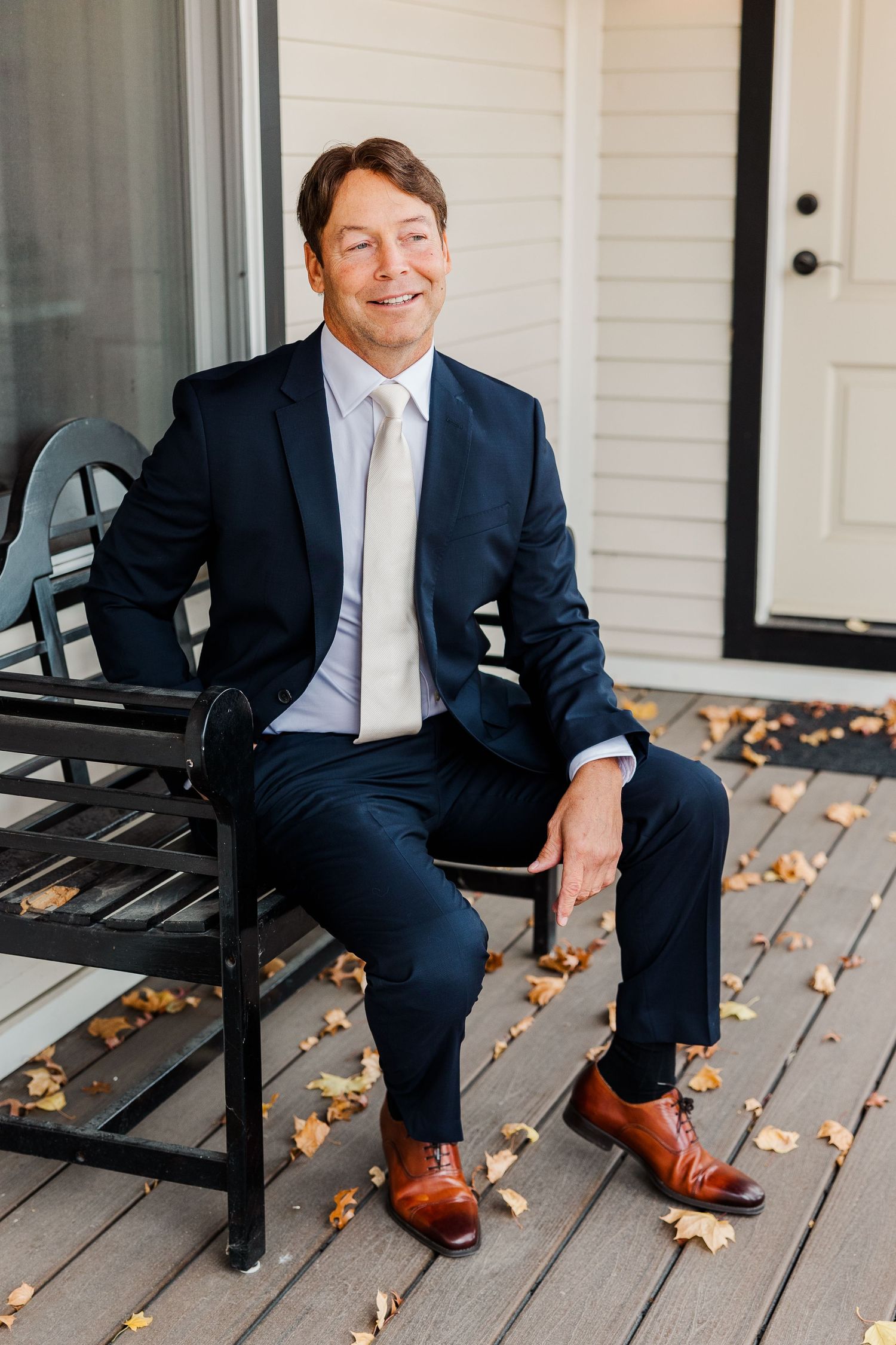 Person in navy suit sitting on black bench with autumn leaves on wooden deck.