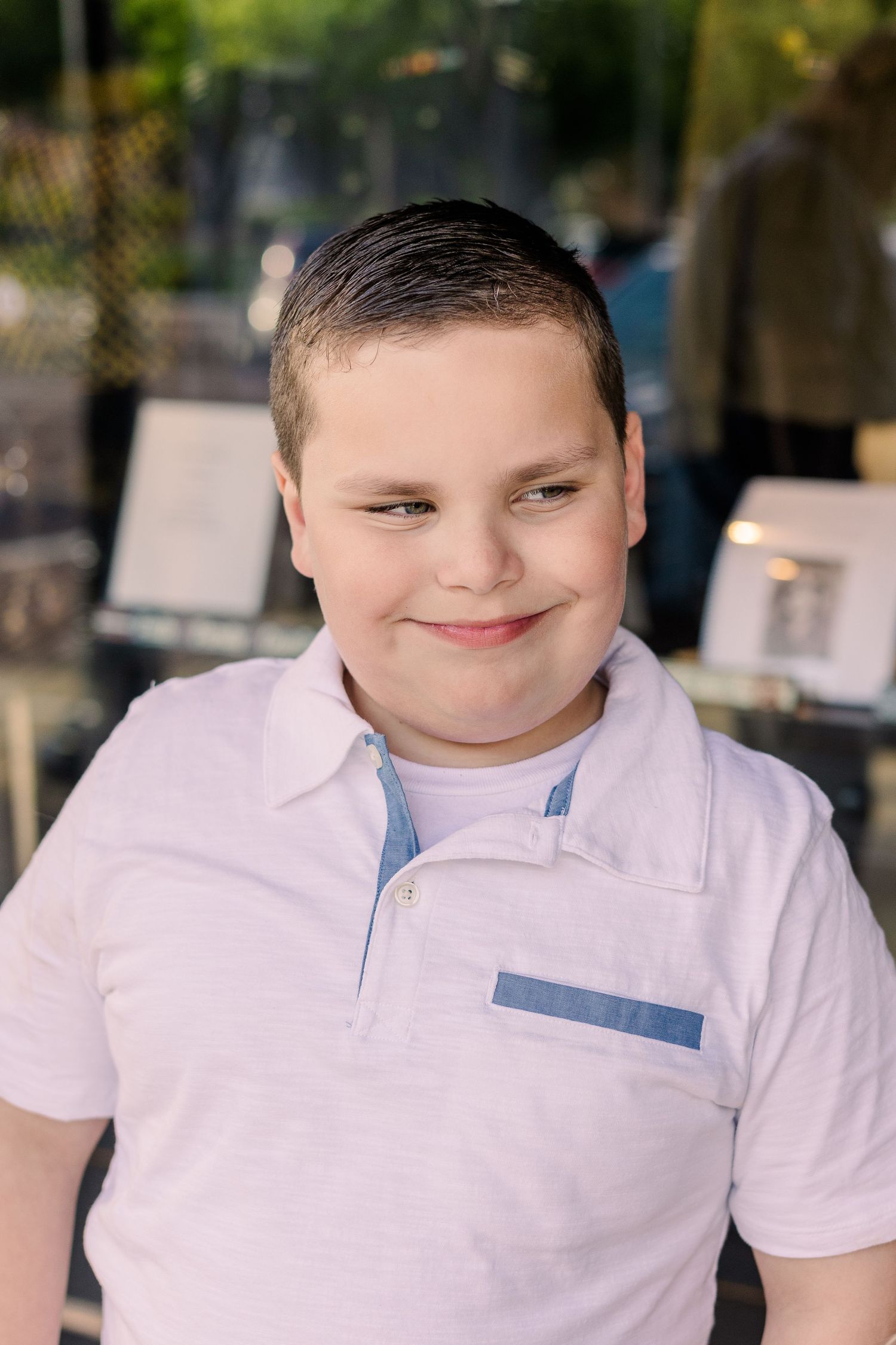 Portrait of youth in white polo shirt with a gentle smile against blurred background.