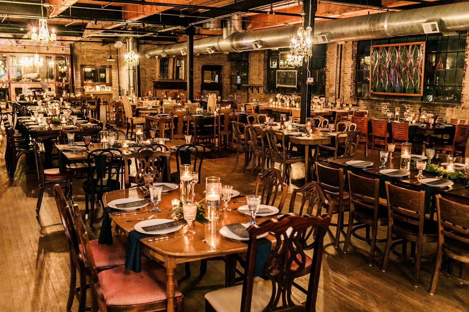 Rustic restaurant interior with wooden tables and chairs illuminated by warm lighting and exposed ceiling beams.