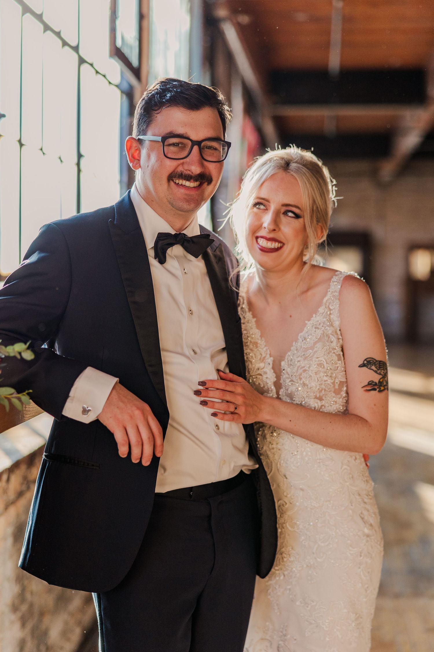 A joyful couple shares a candid moment in an industrial-style wedding venue with natural lighting.
