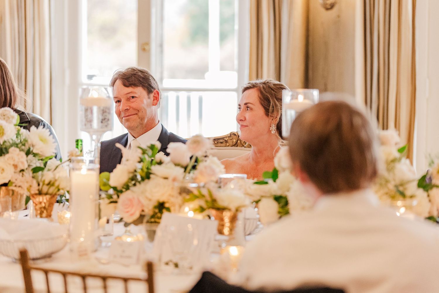 Wedding reception table decorated with elegant white floral centerpieces and glowing candles during dinner.