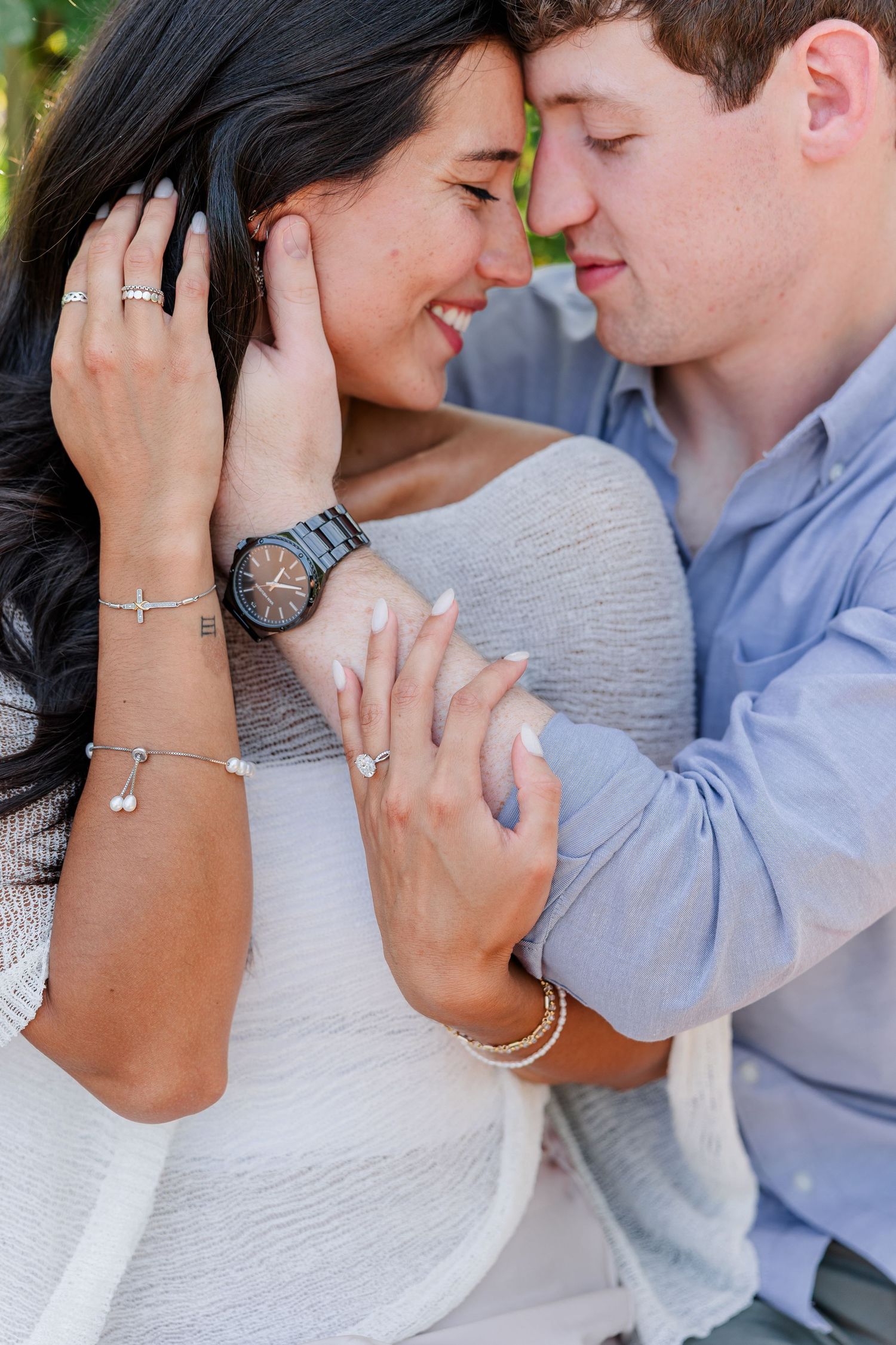 A couple shares an intimate moment, touching foreheads, as the woman displays an engagement ring and elegant jewelry.